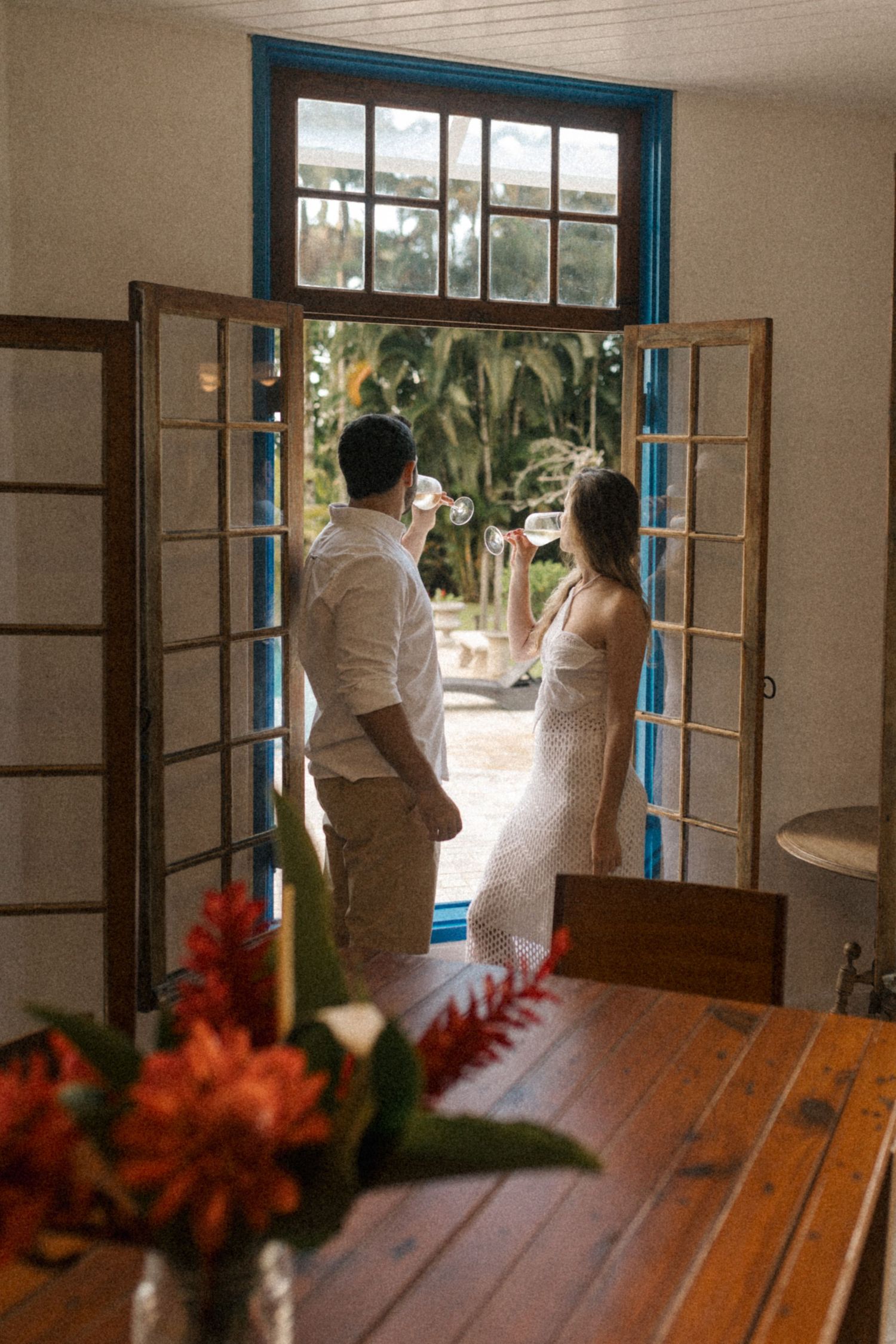A couple shares an intimate moment by French doors with red flowers in the foreground.