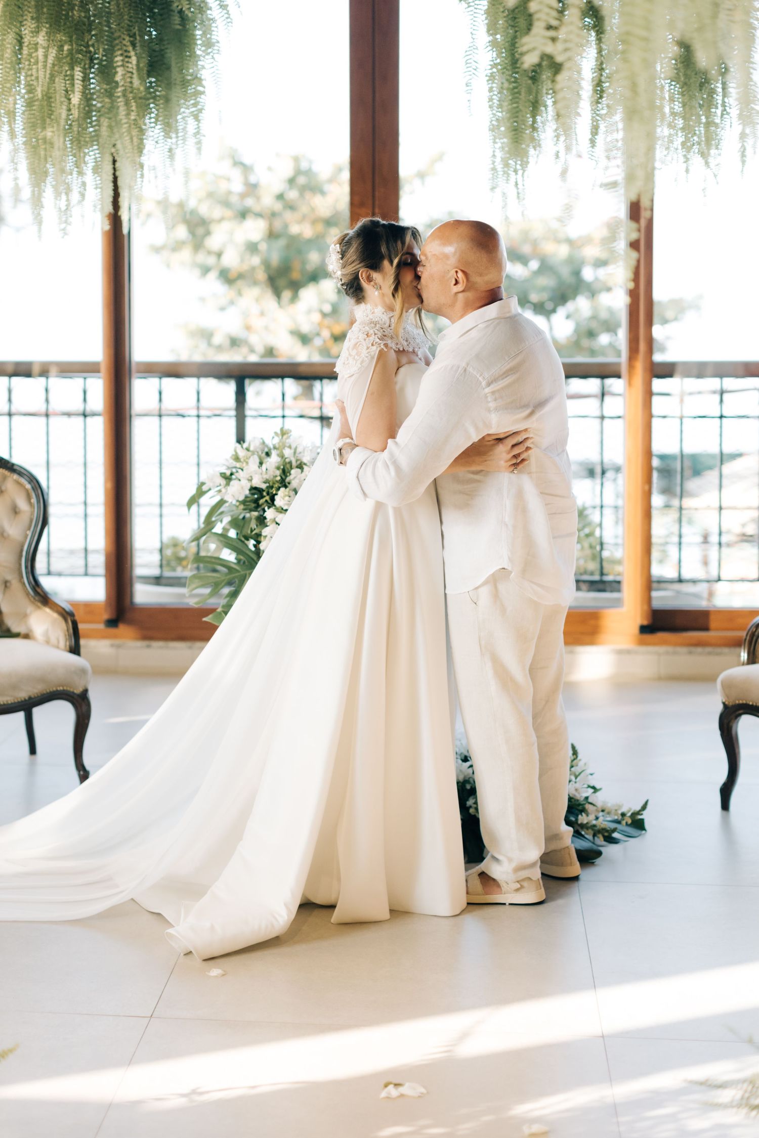 A romantic embrace between newlyweds during their wedding ceremony by large windows.