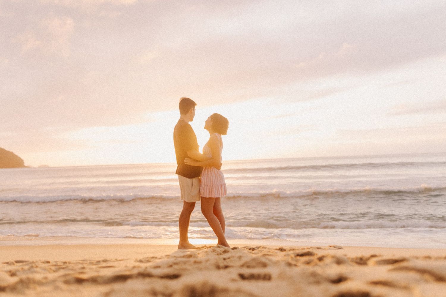 Silhouetted couple shares intimate moment on beach at sunset.
