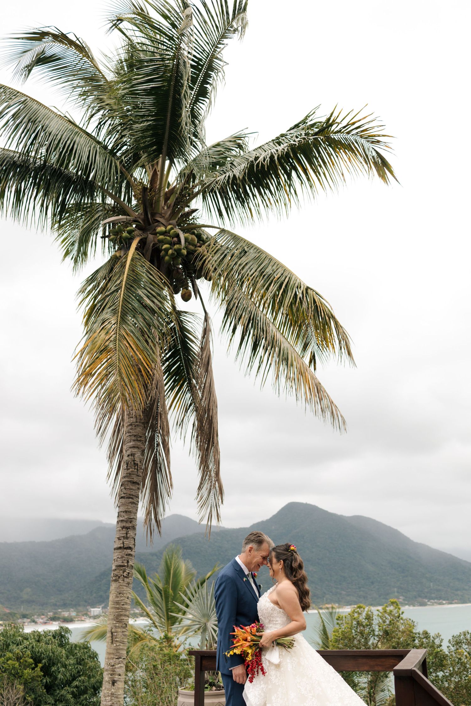 Romantic wedding ceremony under palm trees with mountains and ocean views in the background.