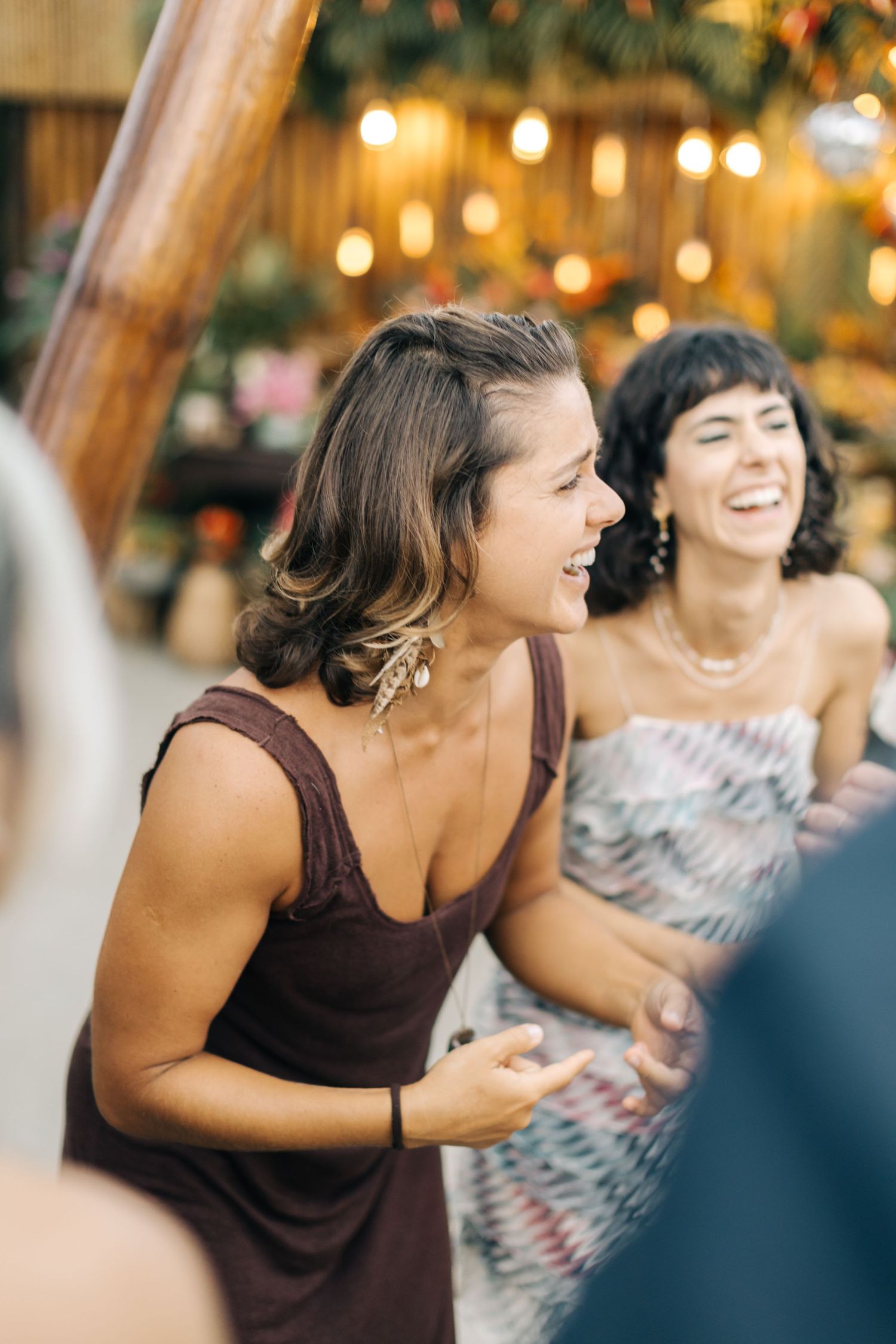 Wedding guests share laughter during an evening reception under warm lighting.
