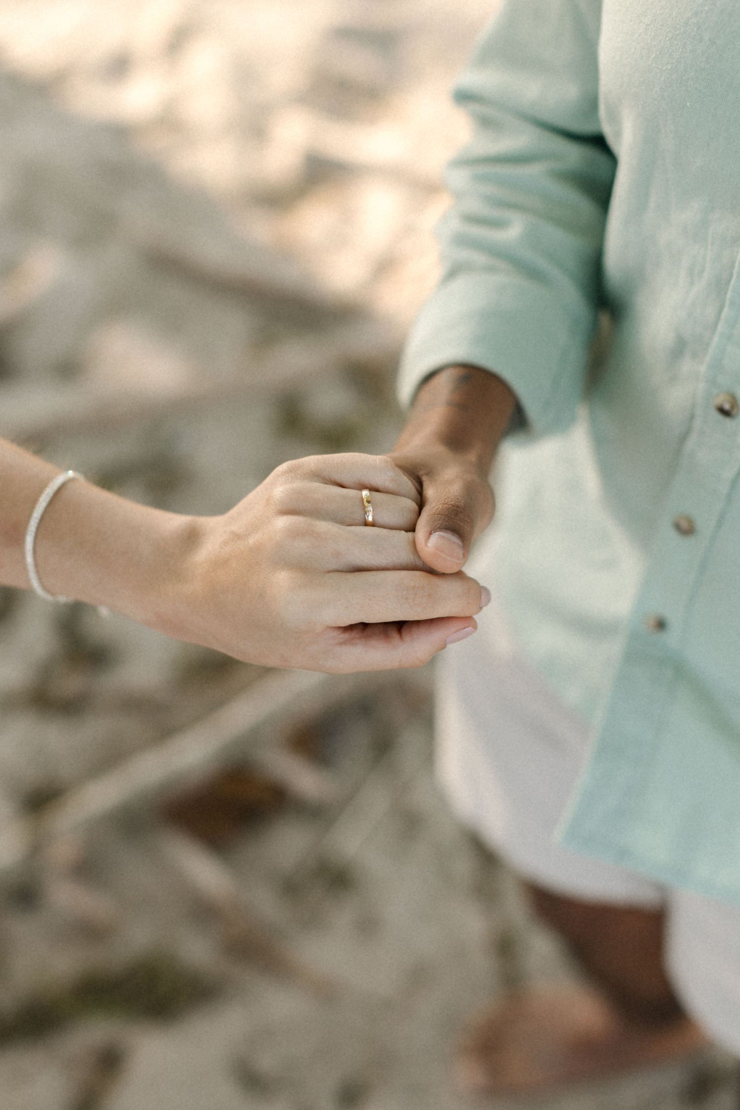 Close-up of hands wearing an engagement ring against a soft blurred background.