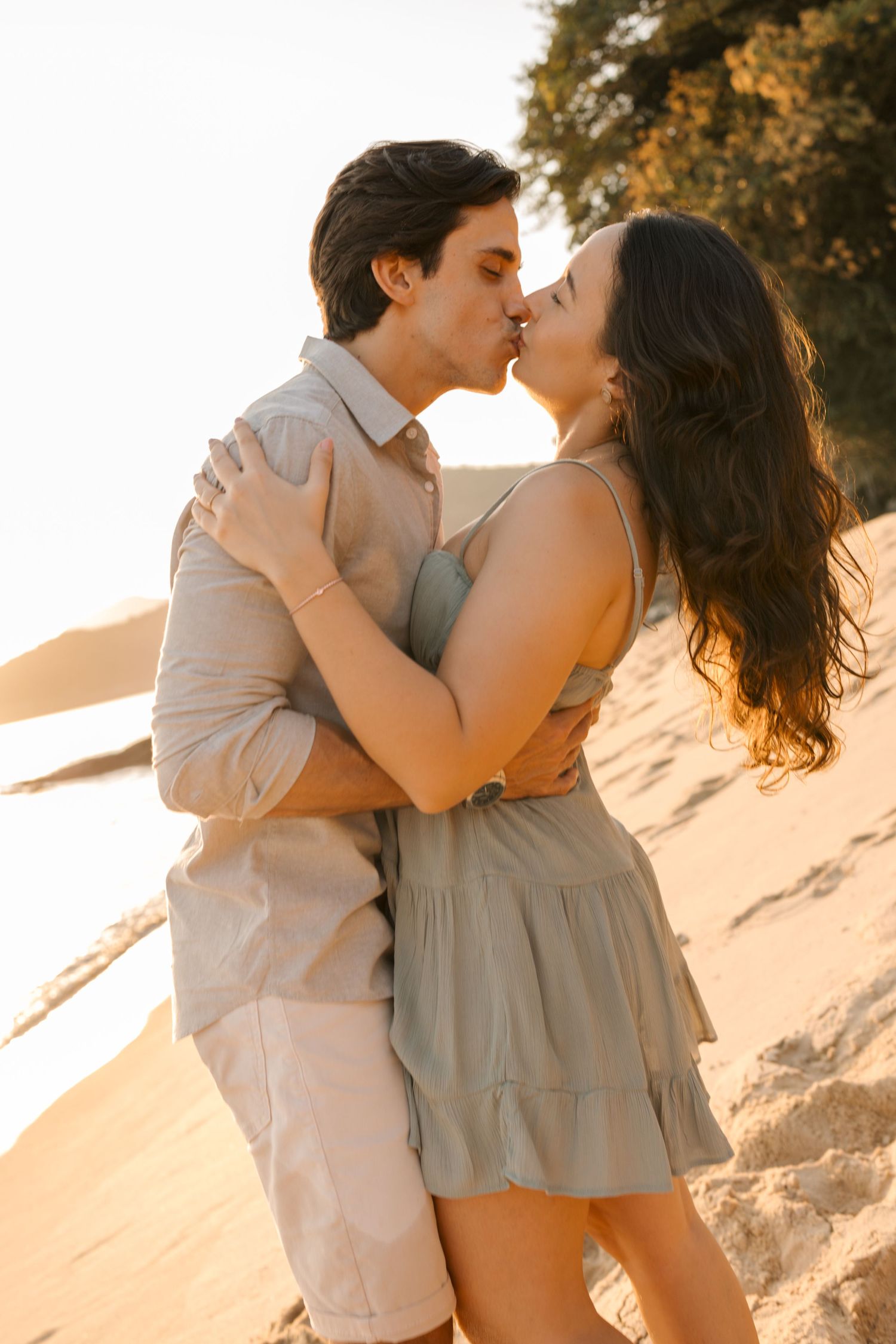 Romantic couple in light colored clothes sharing an intimate moment on a sunlit beach.