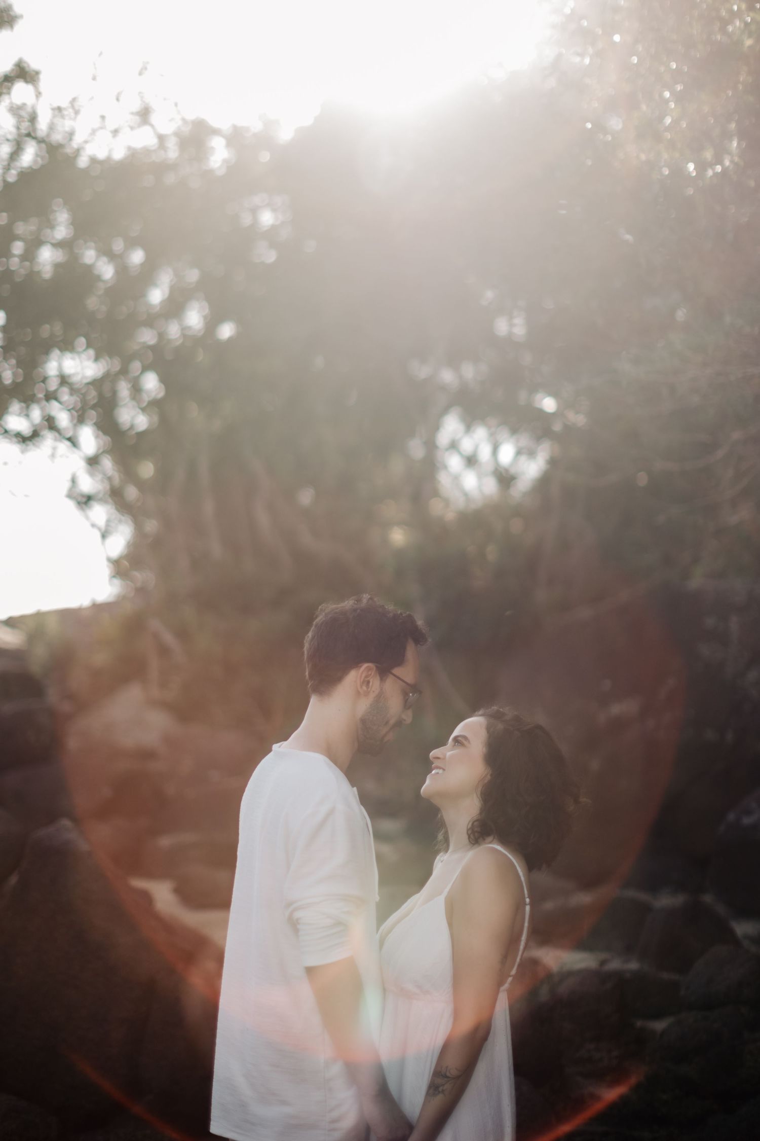 Romantic couple share intimate moment on beach with sunlit hazy background.
