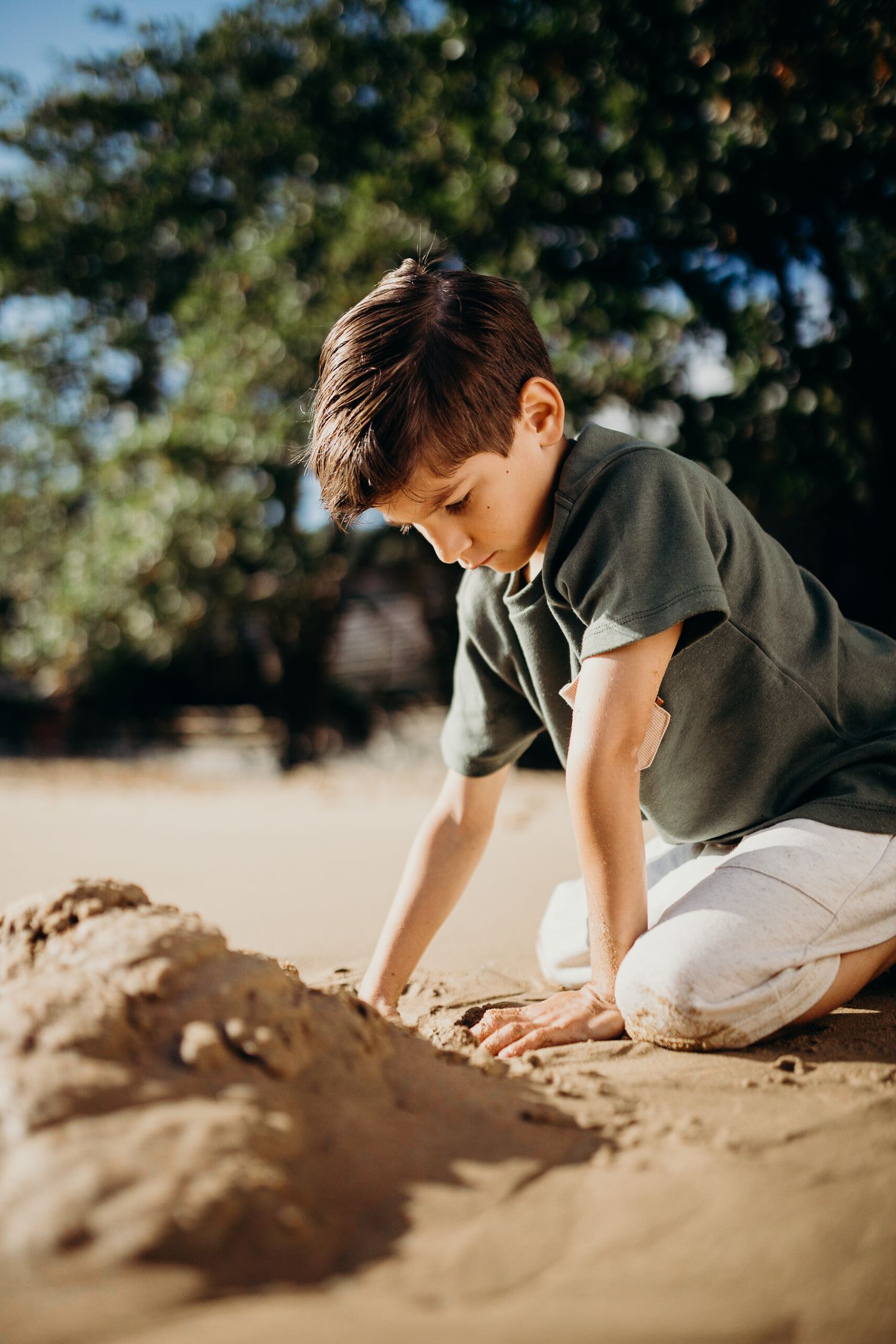Child in grey shirt explores sand formations on tropical beach.