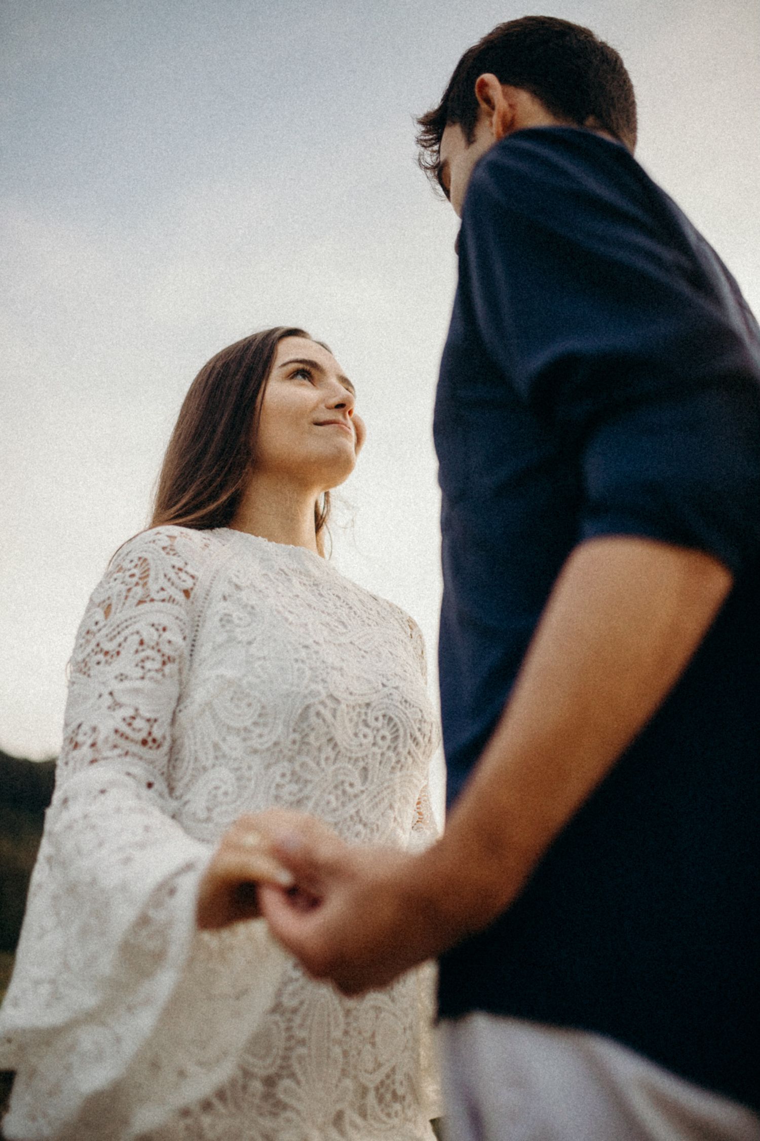 Candid moment between couple in white lace and navy blue during golden hour.