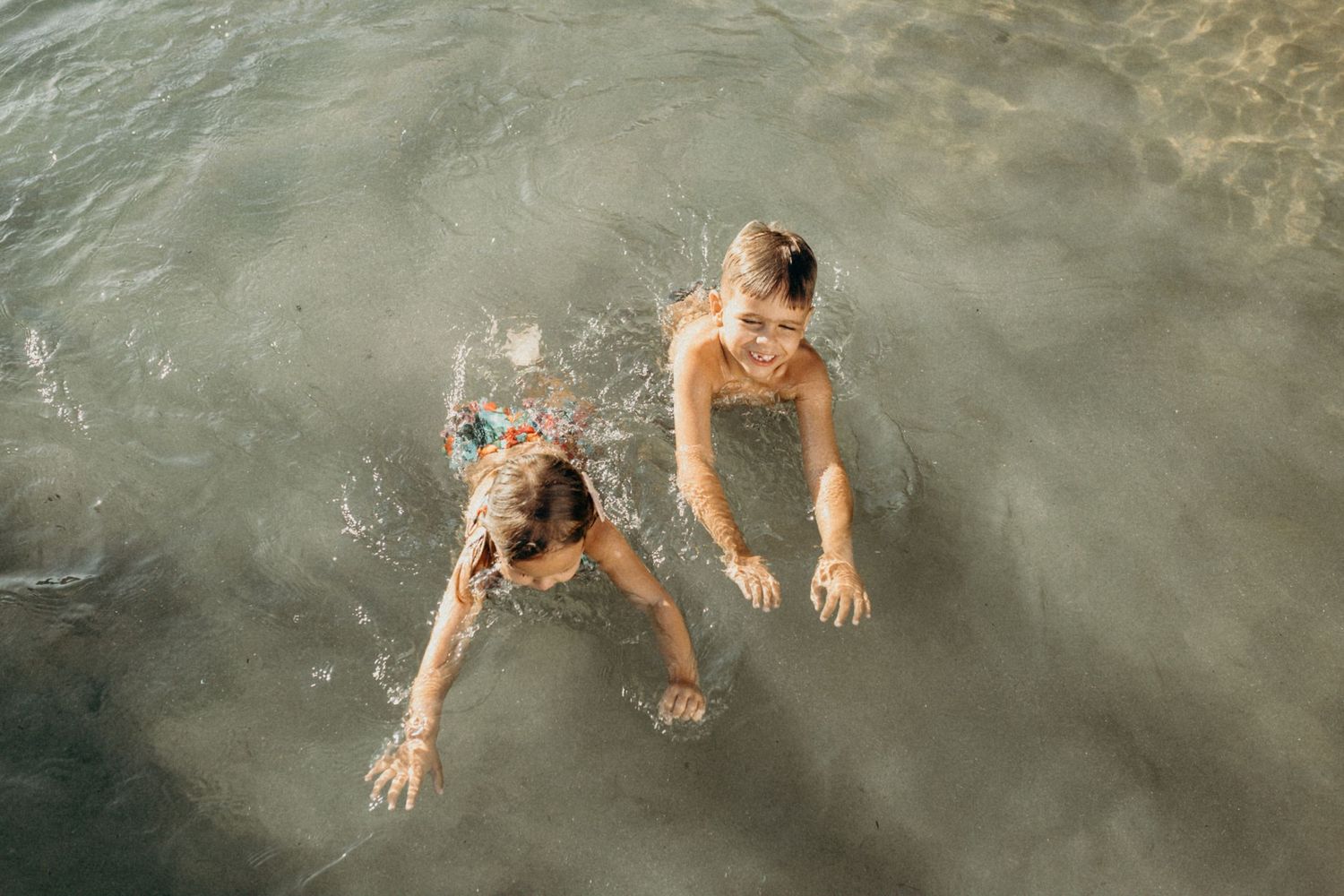 Aerial view of two children swimming in clear ocean water.