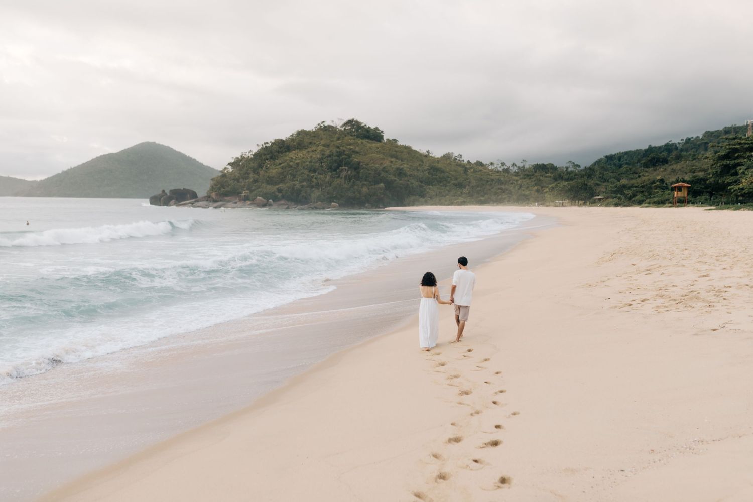 Scenic beach landscape with mountains in the distance and footprints in the sand.