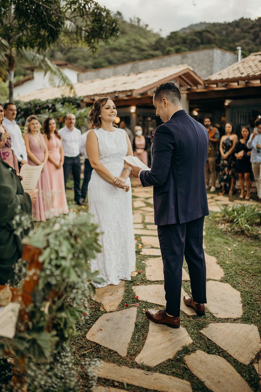 A wedding ceremony takes place on a rustic stone pathway with mountains and greenery in the background.