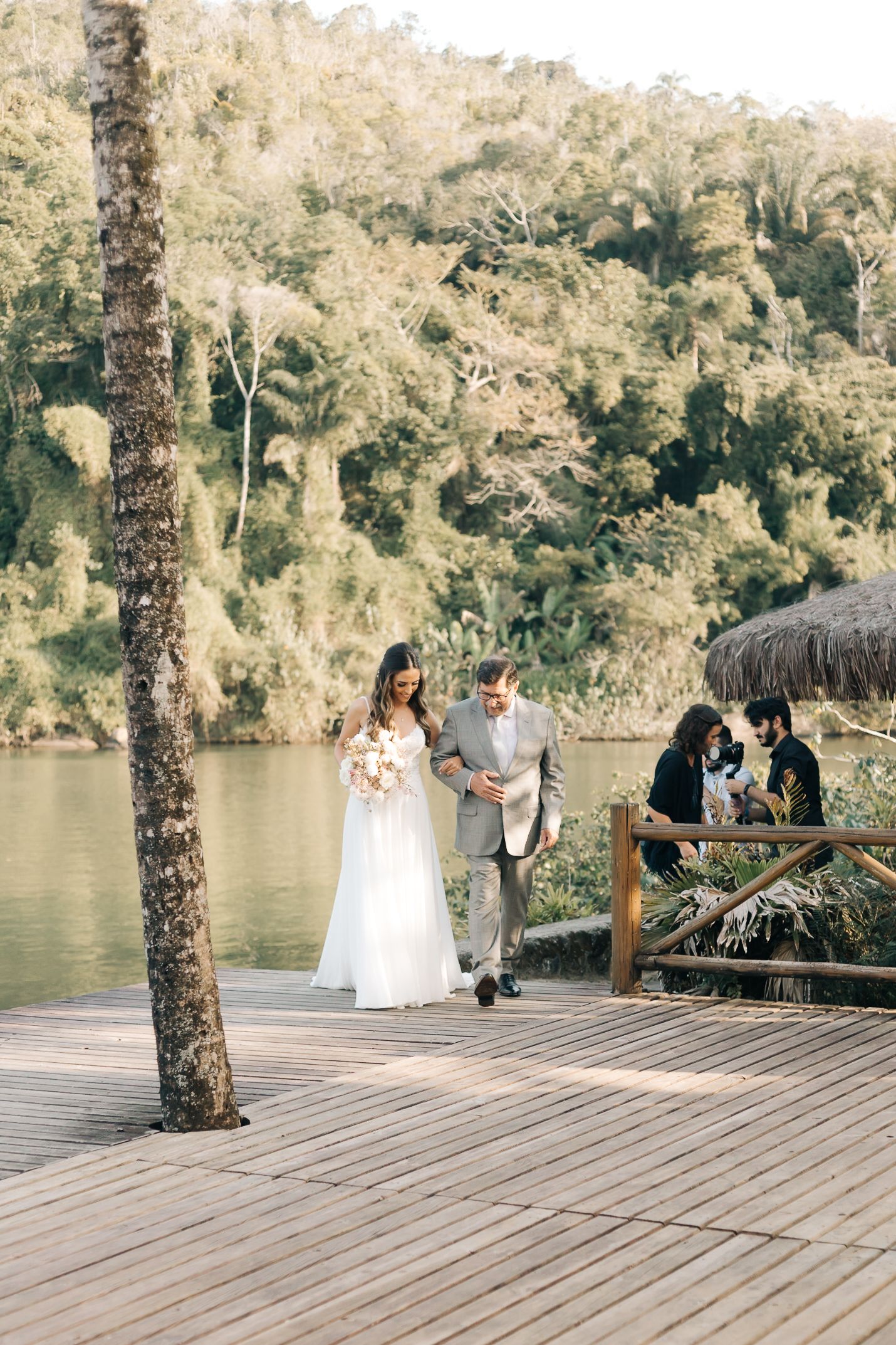 Outdoor lakeside wedding ceremony on wooden deck surrounded by lush forest scenery.