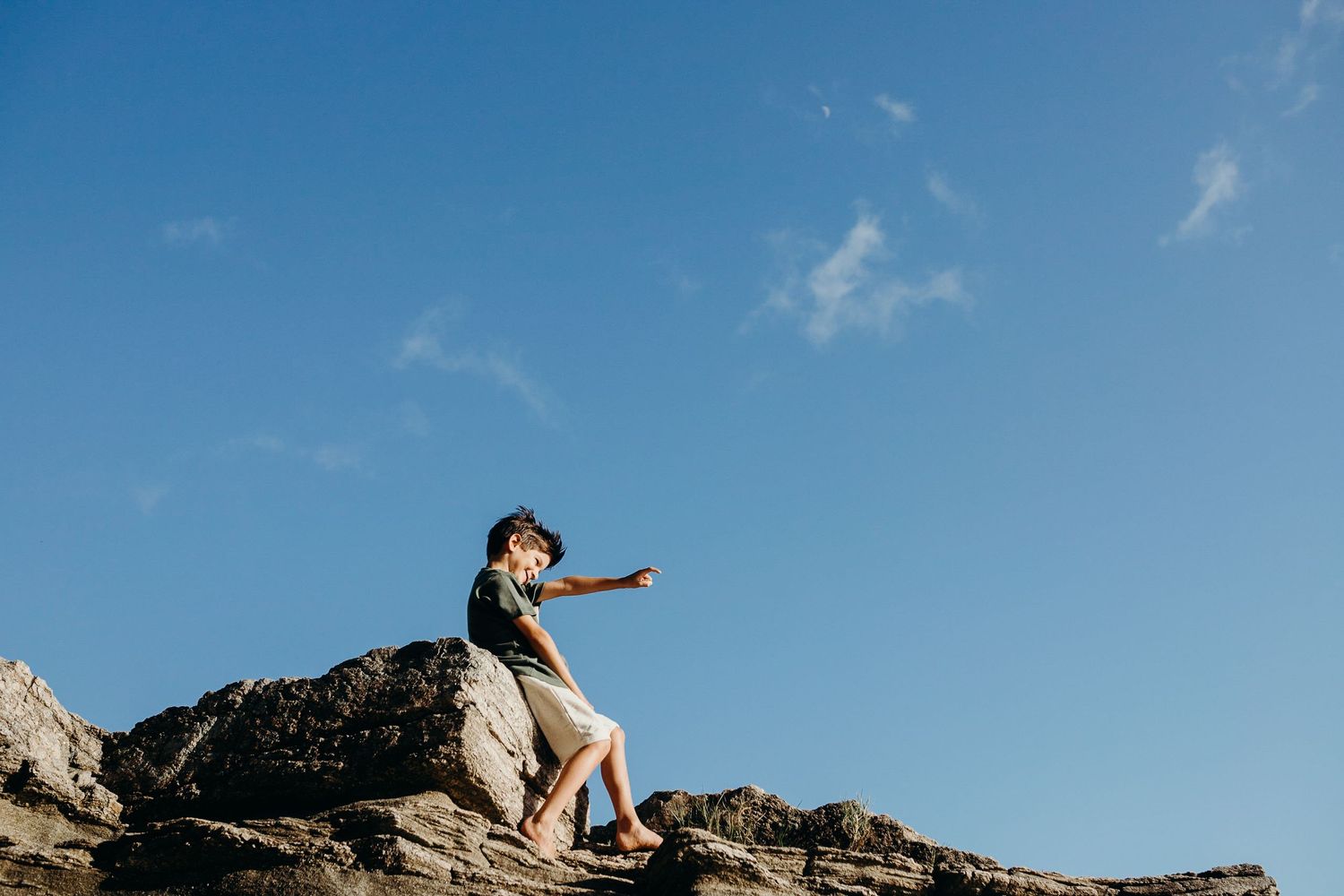 Person points towards horizon while perched on rocky seaside cliff.