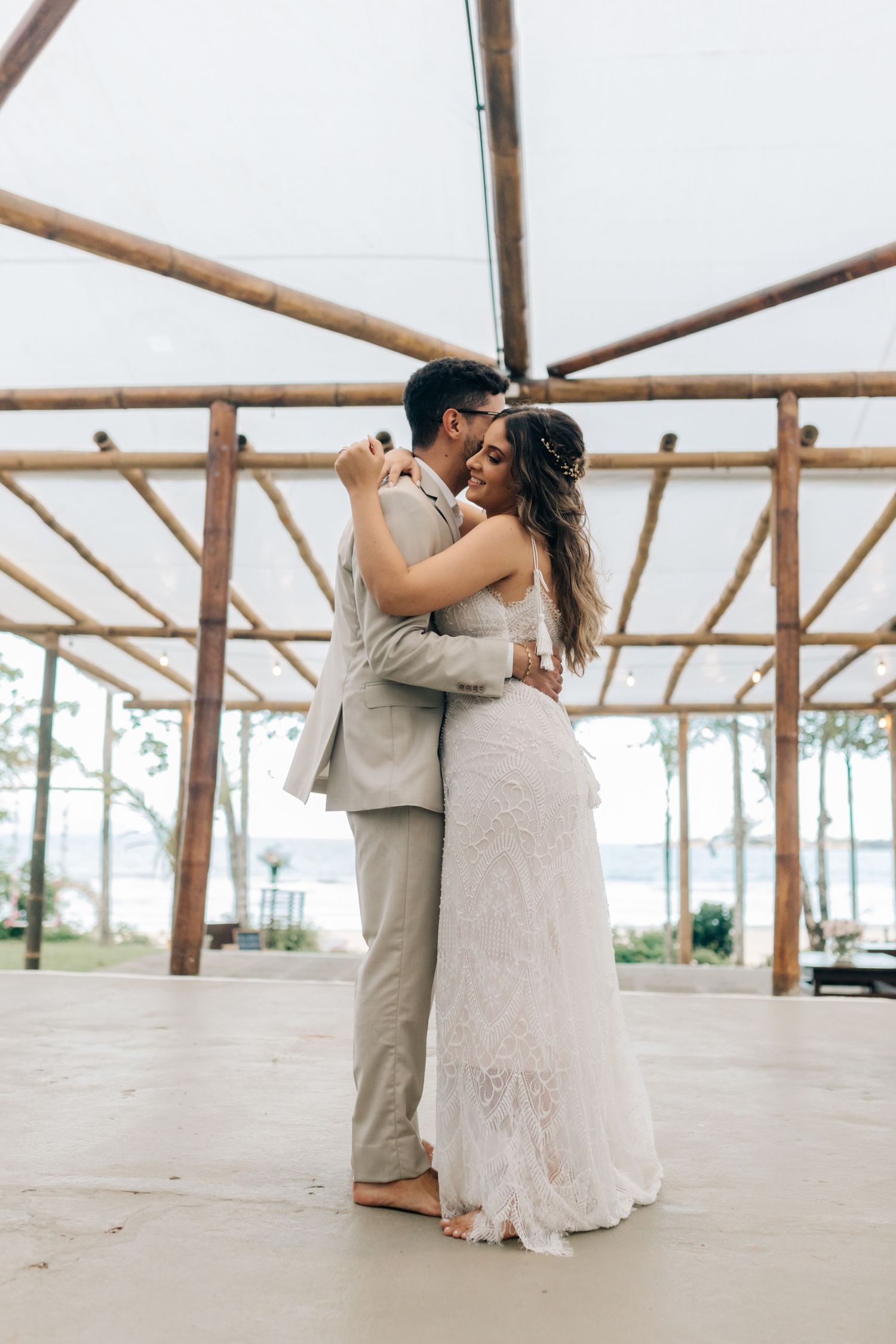 A couple shares an intimate dance moment under a rustic beach pavilion.