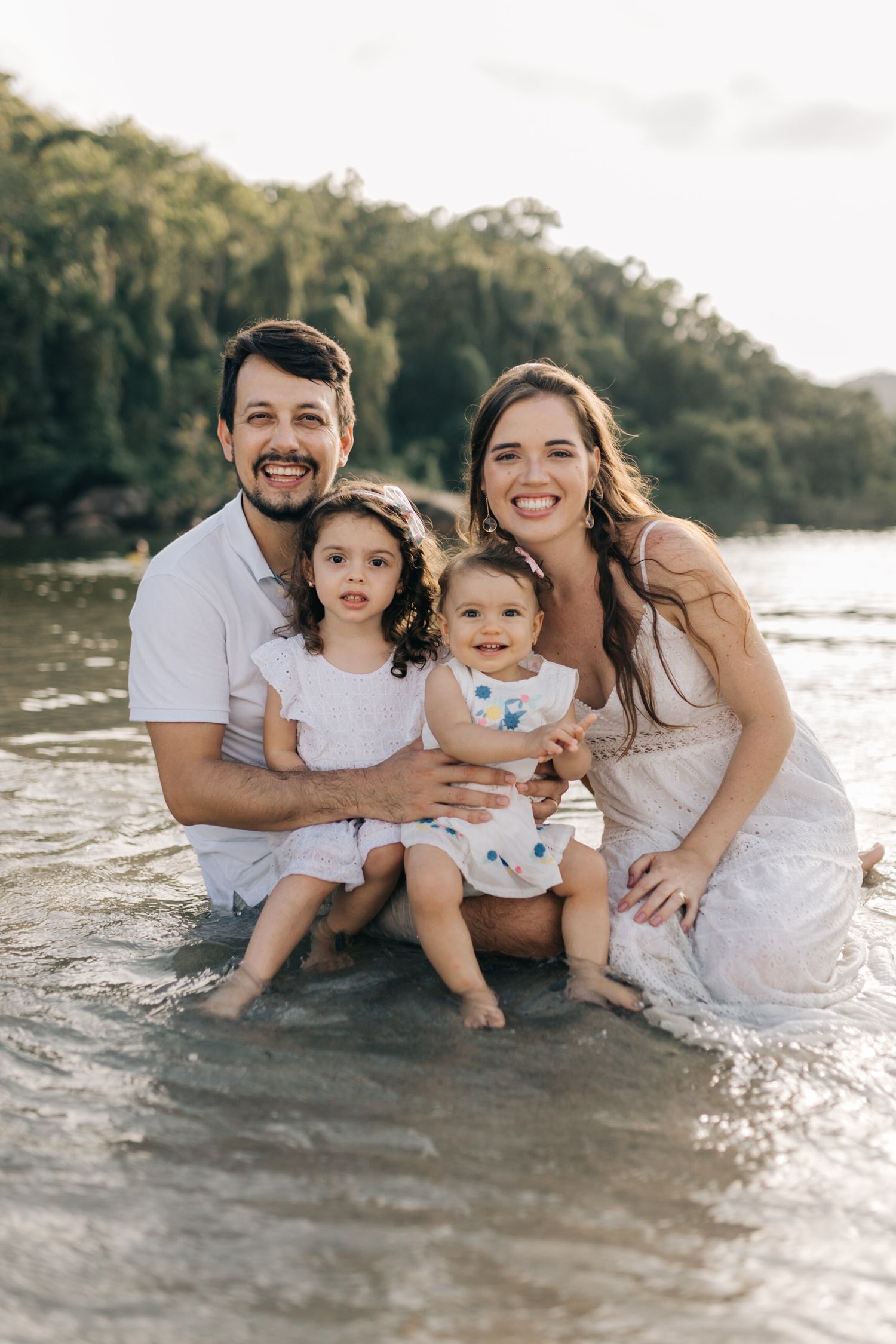 A family portrait at the lake with everyone wearing white and smiling at the camera.