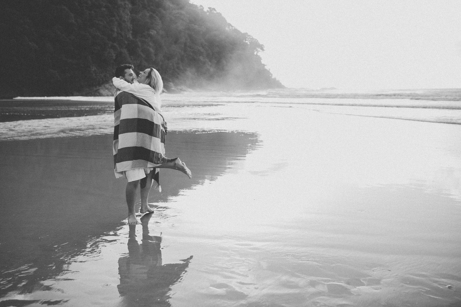 Two figures walk along a serene beach shoreline with gentle waves crashing at their feet.