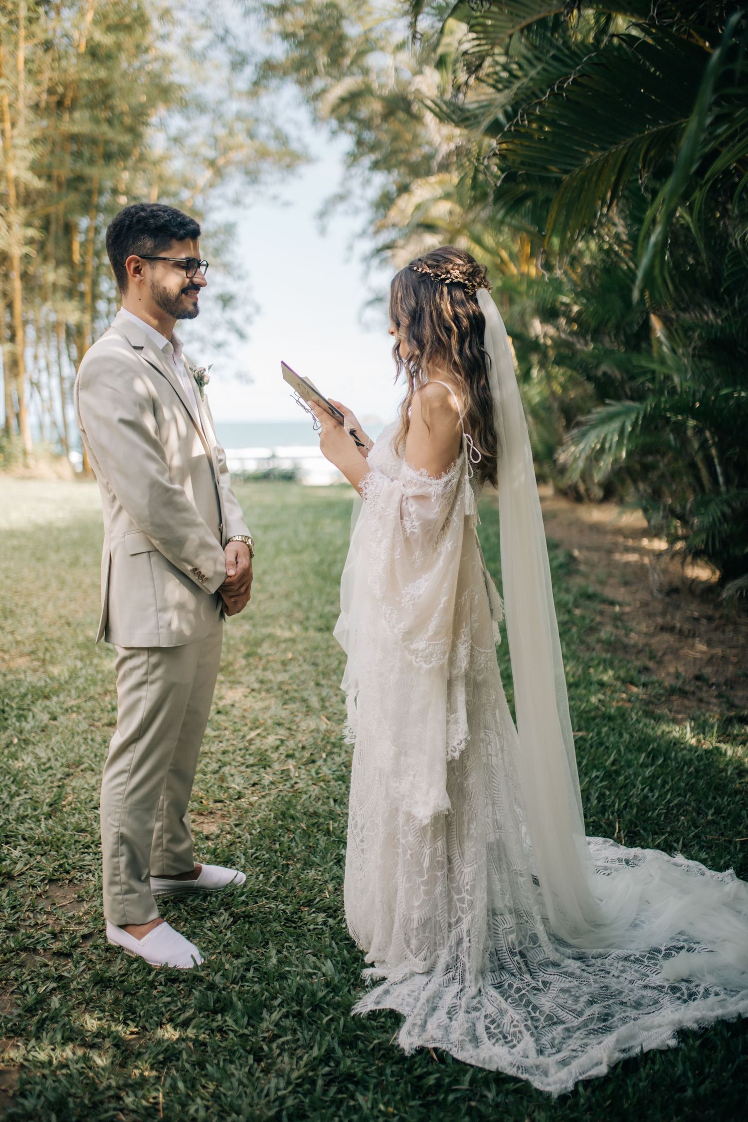 Couple reading personal vows during their outdoor wedding with tropical foliage backdrop.