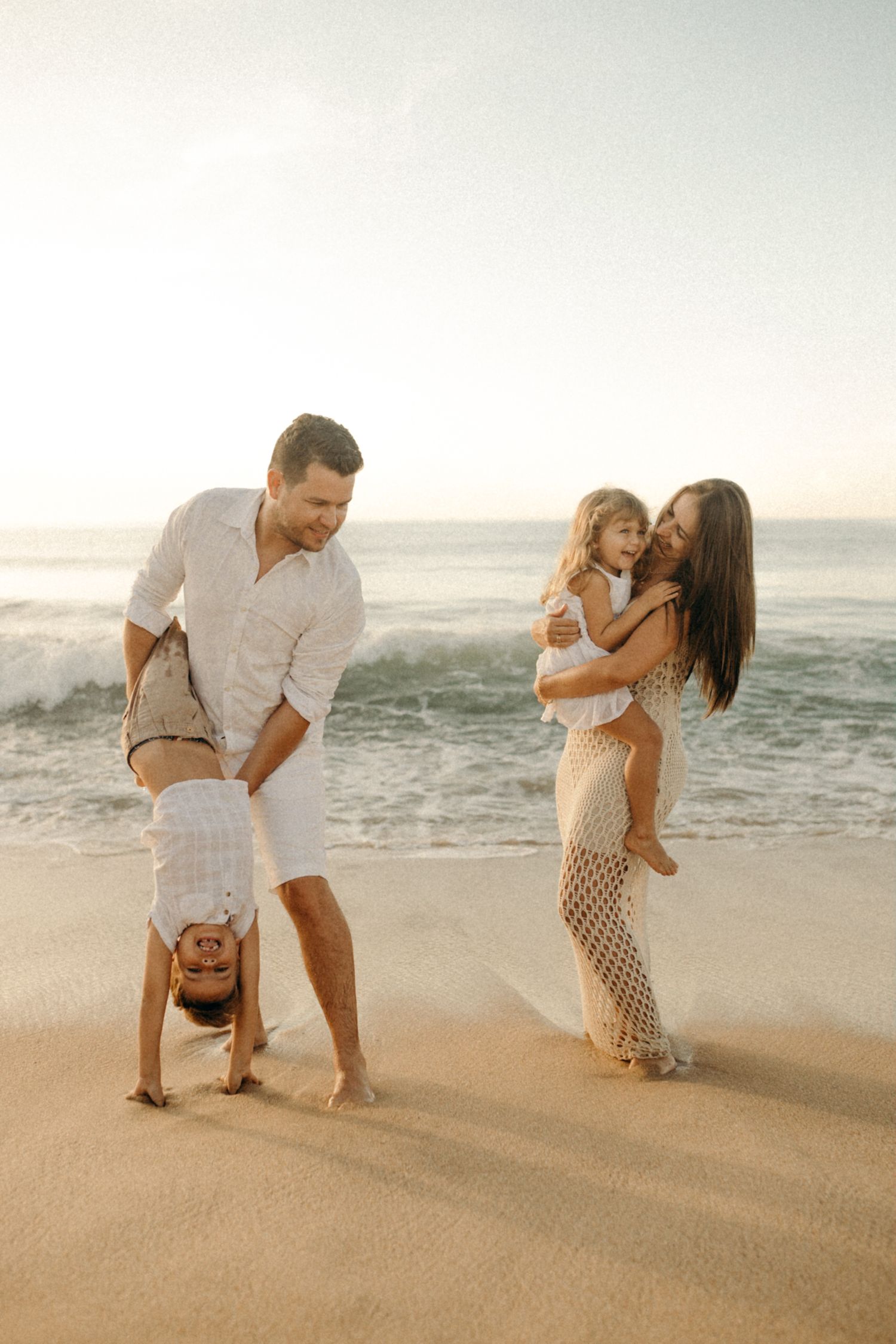 Family playing and doing handstands together on beach at sunset.