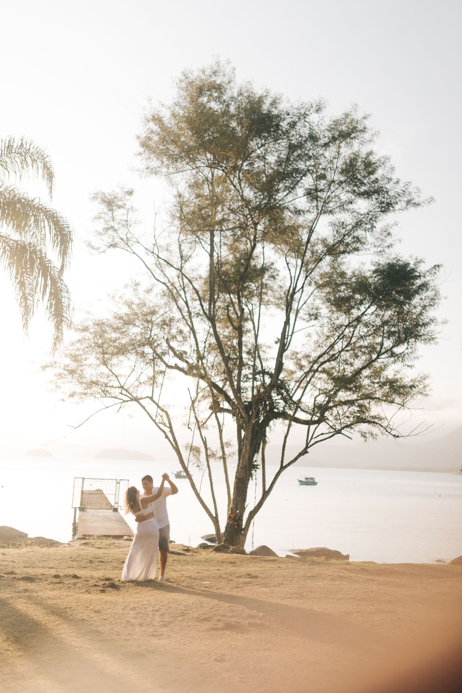 A couple dancing together on a hilltop near a large tree with ocean views.