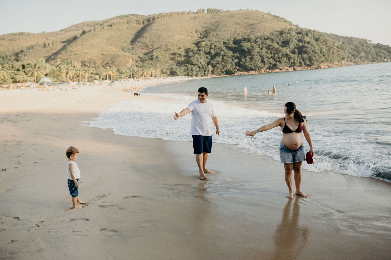 A family plays together at the water's edge on a scenic beach.