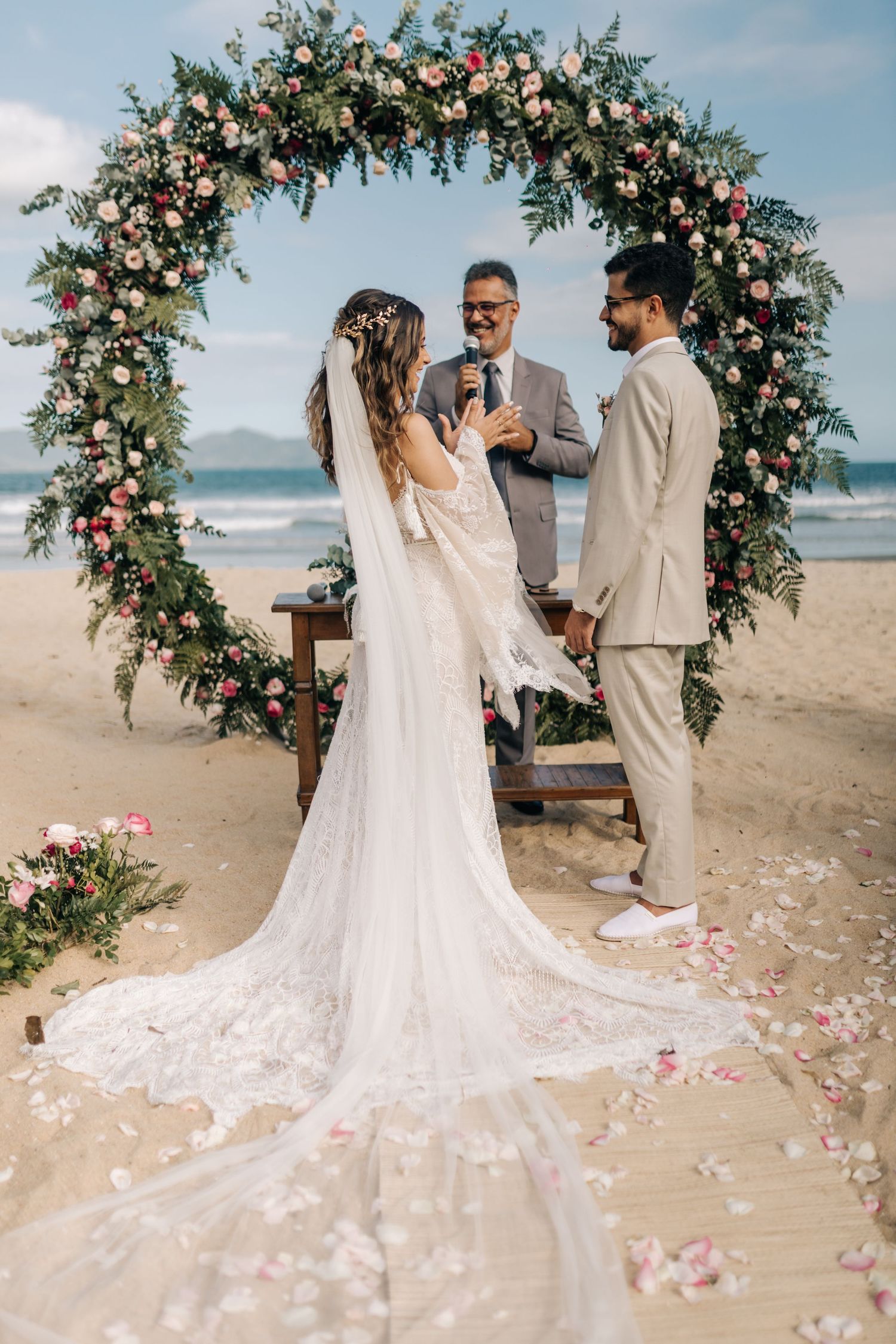 A beach wedding ceremony captures the exchange of vows under a stunning floral arch.