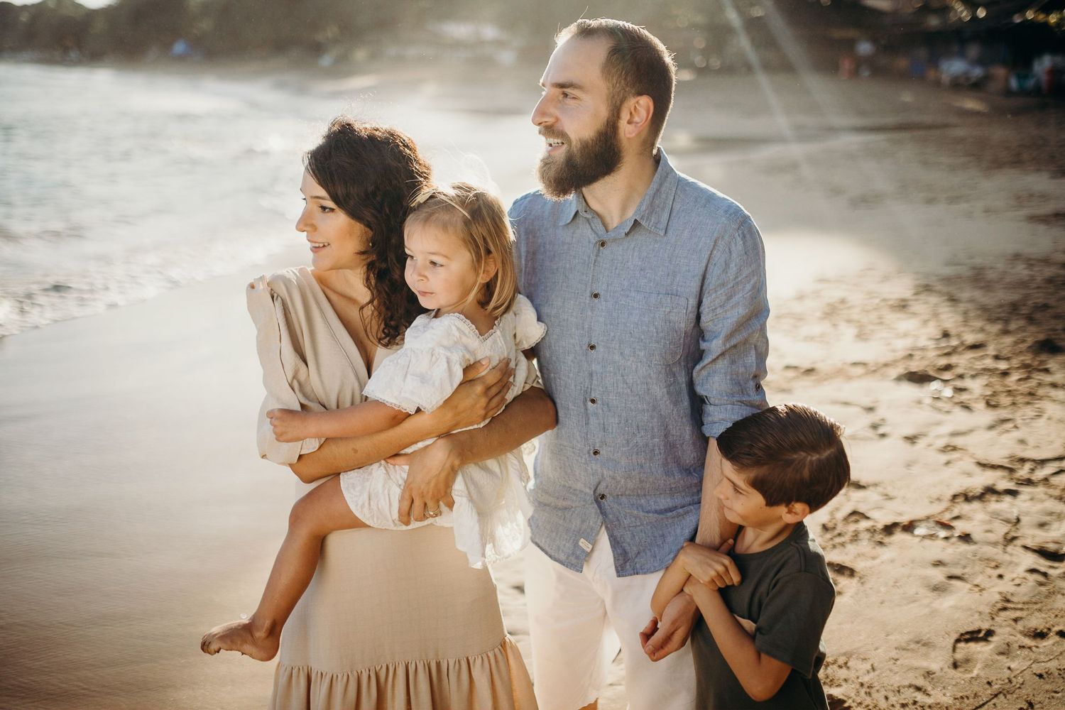 A family shares a tender moment together on a sandy beach at sunset.