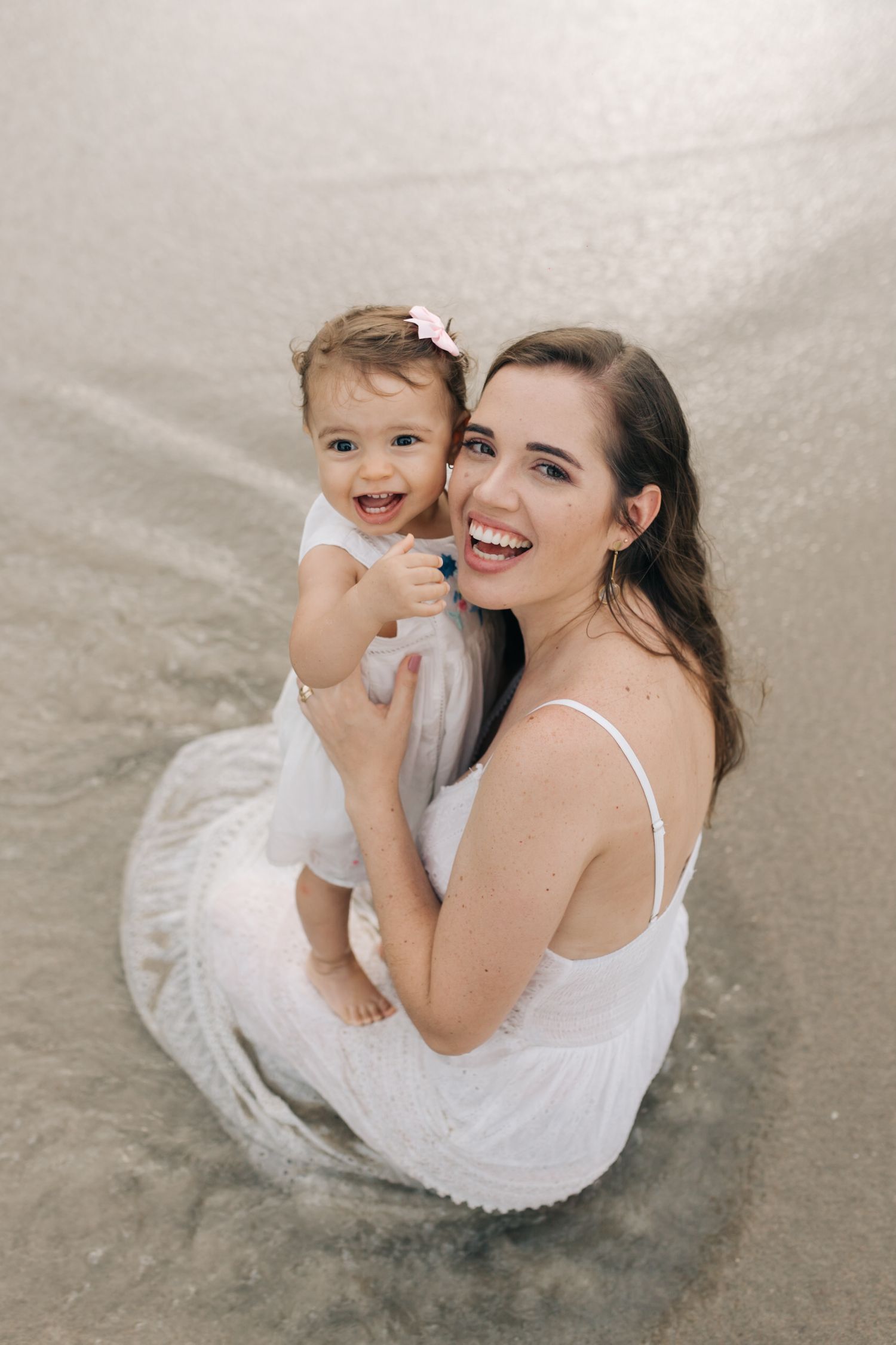 A tender moment captured between family members in white attire at the beach.