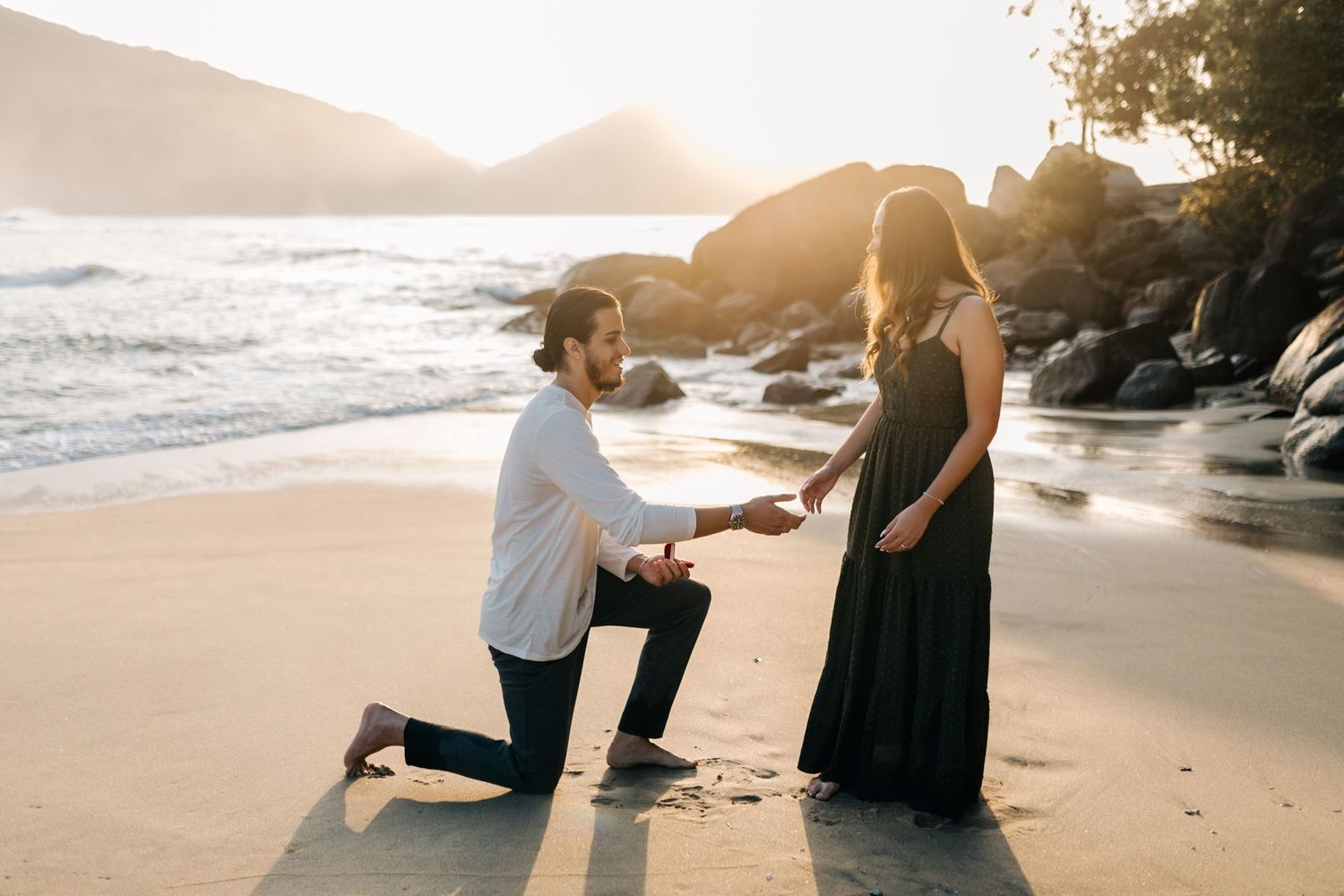 Beautiful beach engagement scene with mountains and ocean waves at sunset.