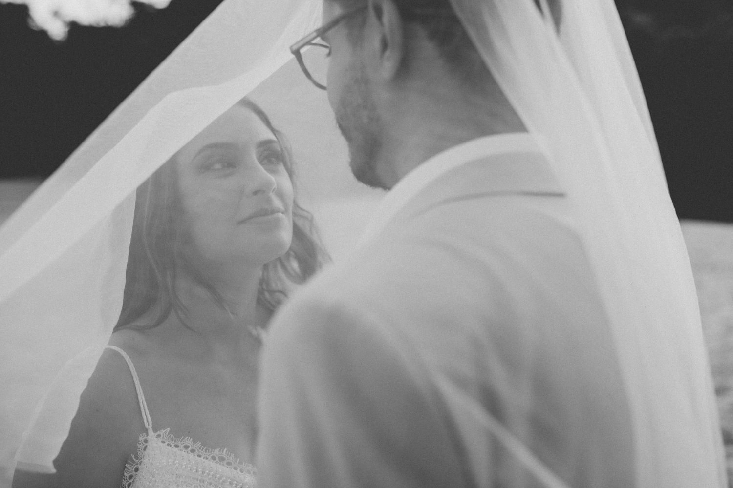 Black and white wedding portrait of newlyweds sharing a tender moment beneath a delicate veil.