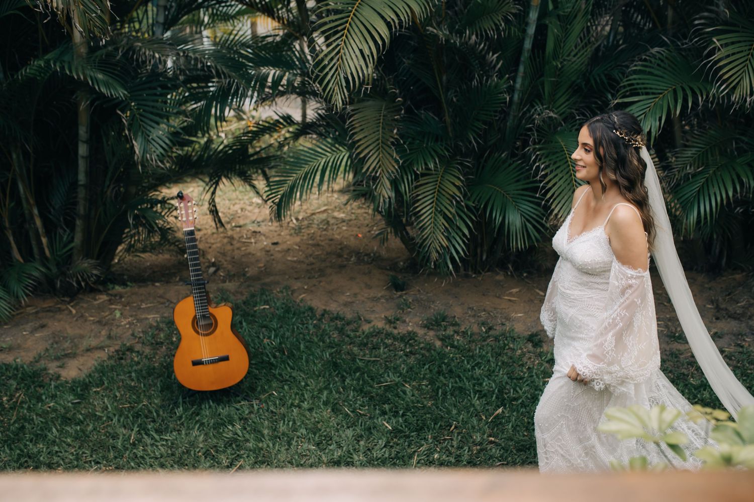 A bride in a white gown poses in a garden setting with an acoustic guitar in the background.