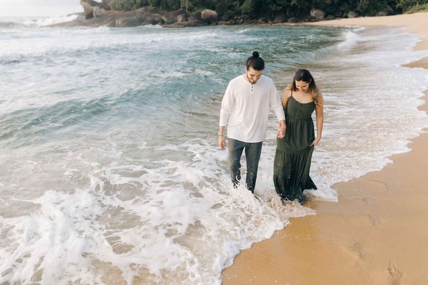 Couple walking in the shallow surf on a tropical beach with waves rolling in.