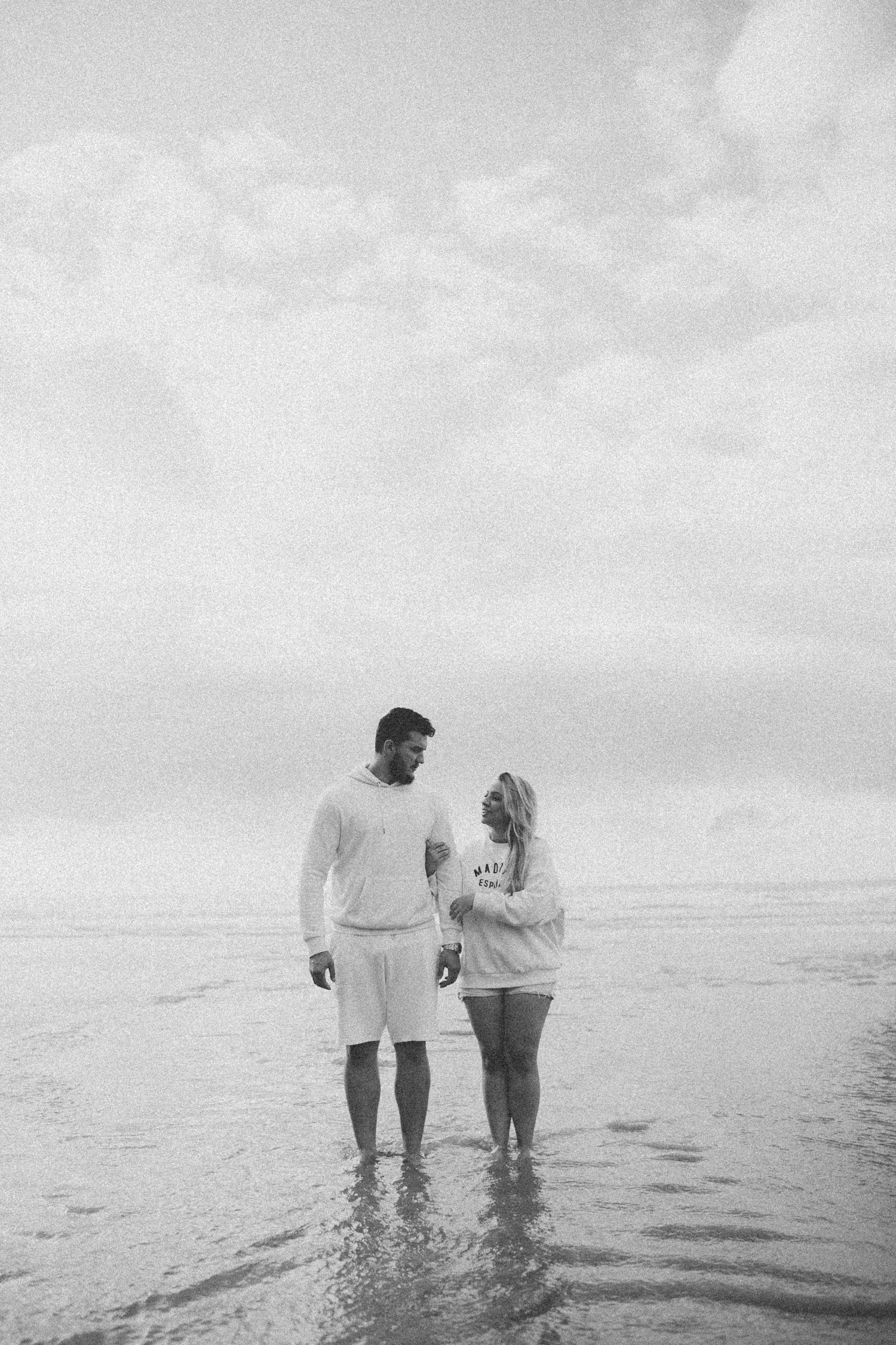 Black and white photo of couple standing together at the ocean's edge.