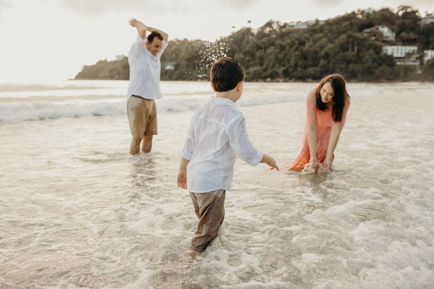 Three people playing and splashing in the shallow ocean water at sunset.