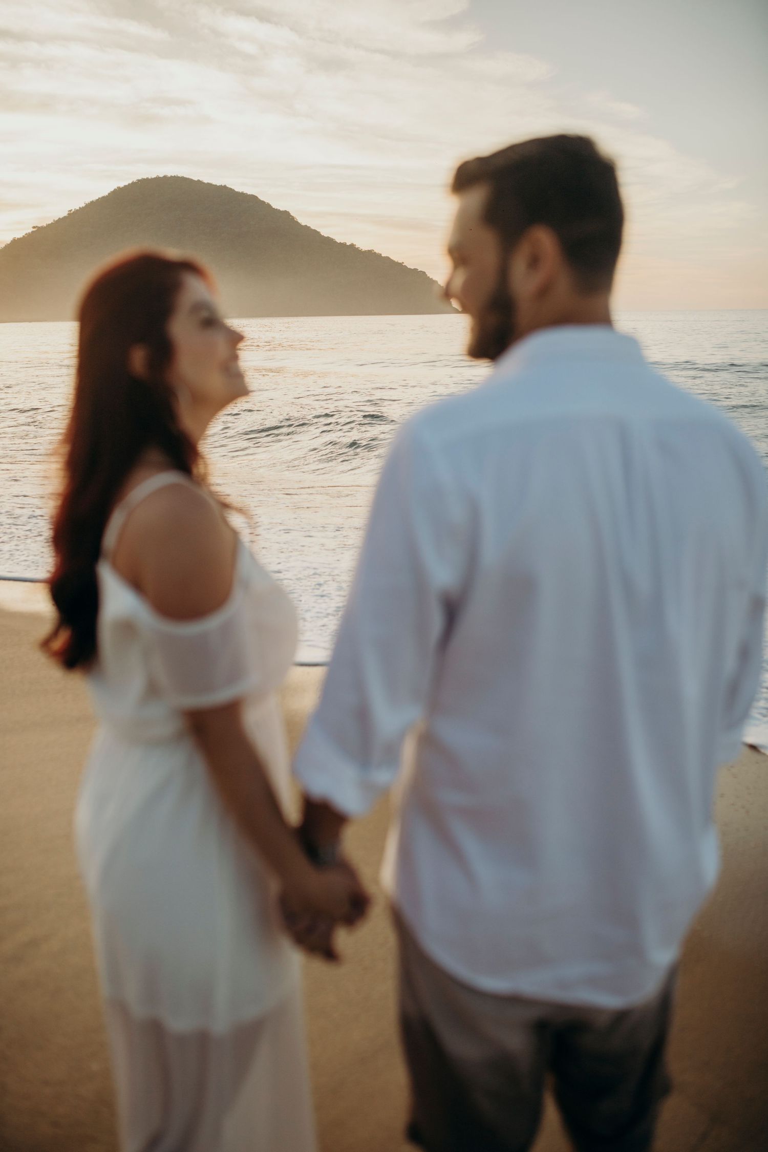 Two people hold hands while enjoying a sunset moment on the beach.