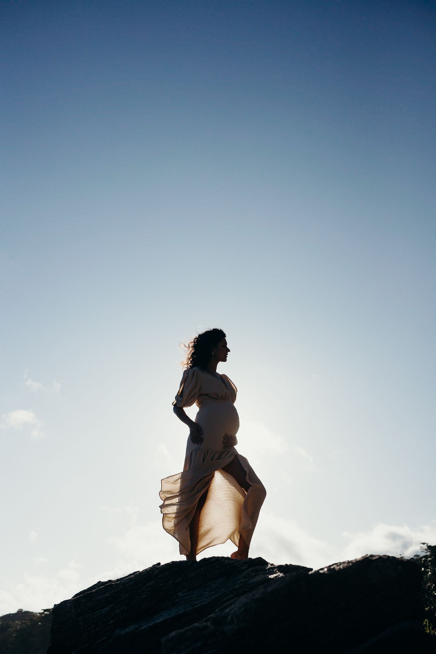 Silhouetted figure in flowing dress stands confidently on rocky outcrop.