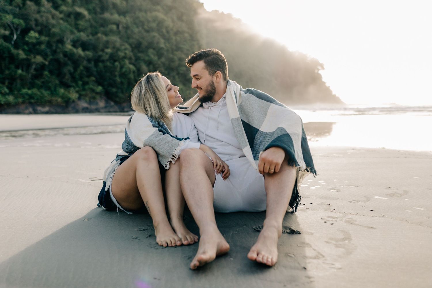 Intimate moment shared between couple sitting on beach with coastal cliffs in background.