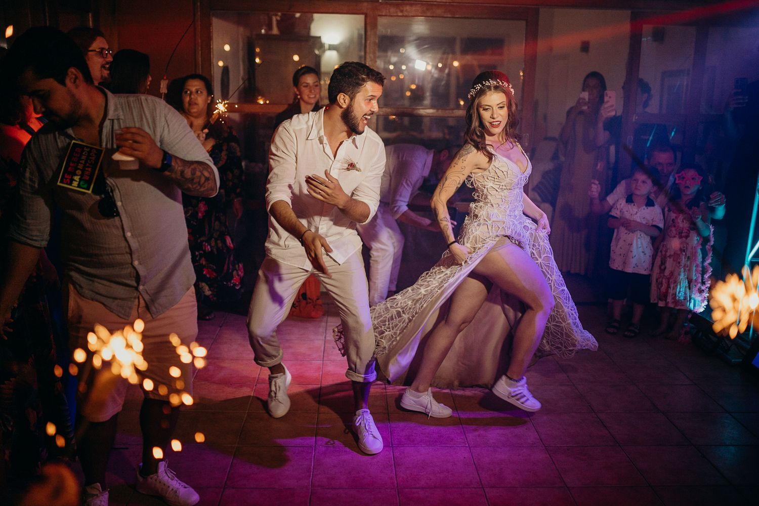 Wedding guests performing synchronized dance moves under dramatic purple lighting.