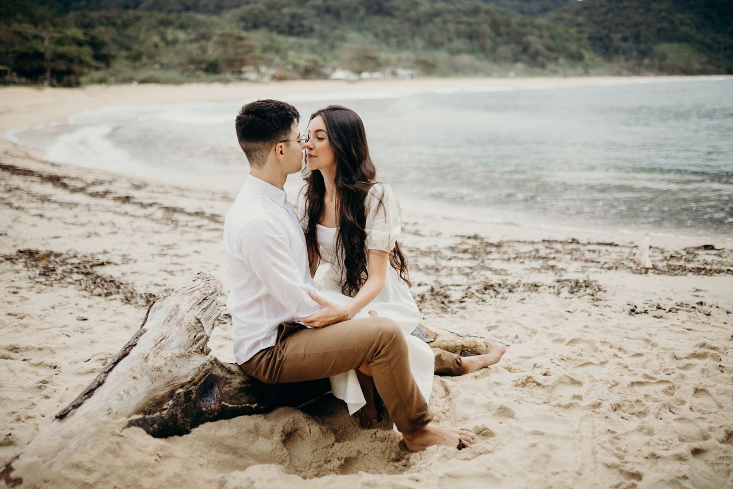 Romantic beach photoshoot with couple sitting on sandy shore.