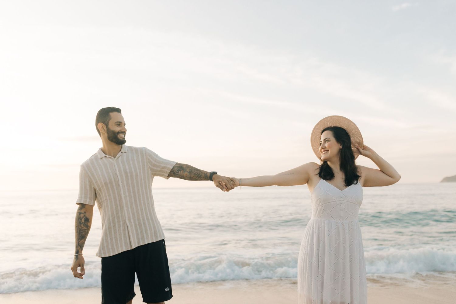 Couple holds hands and dances on the beach during a dreamy sunset photoshoot.