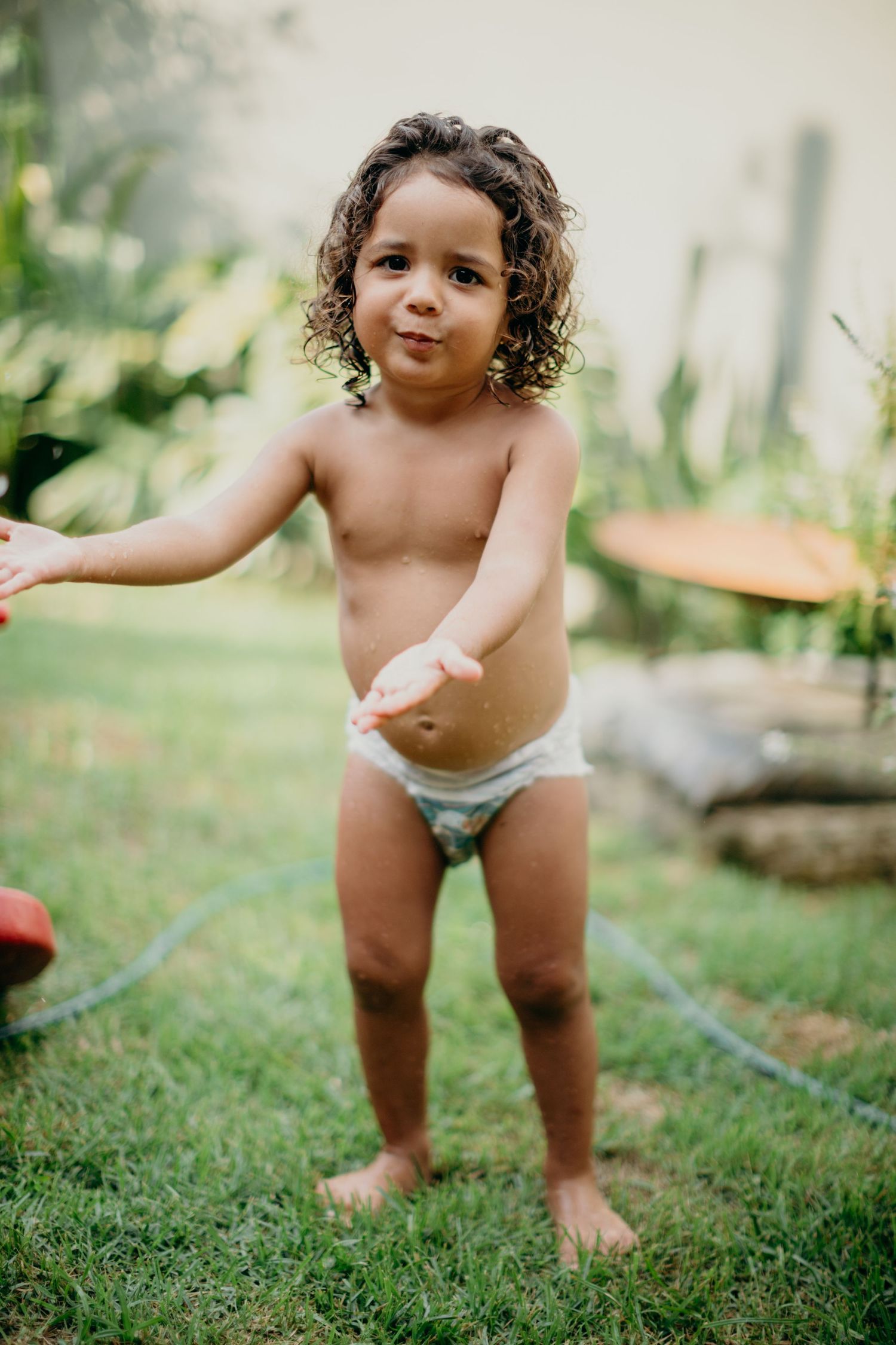 A curly-haired toddler stands on grass while playing outdoors.