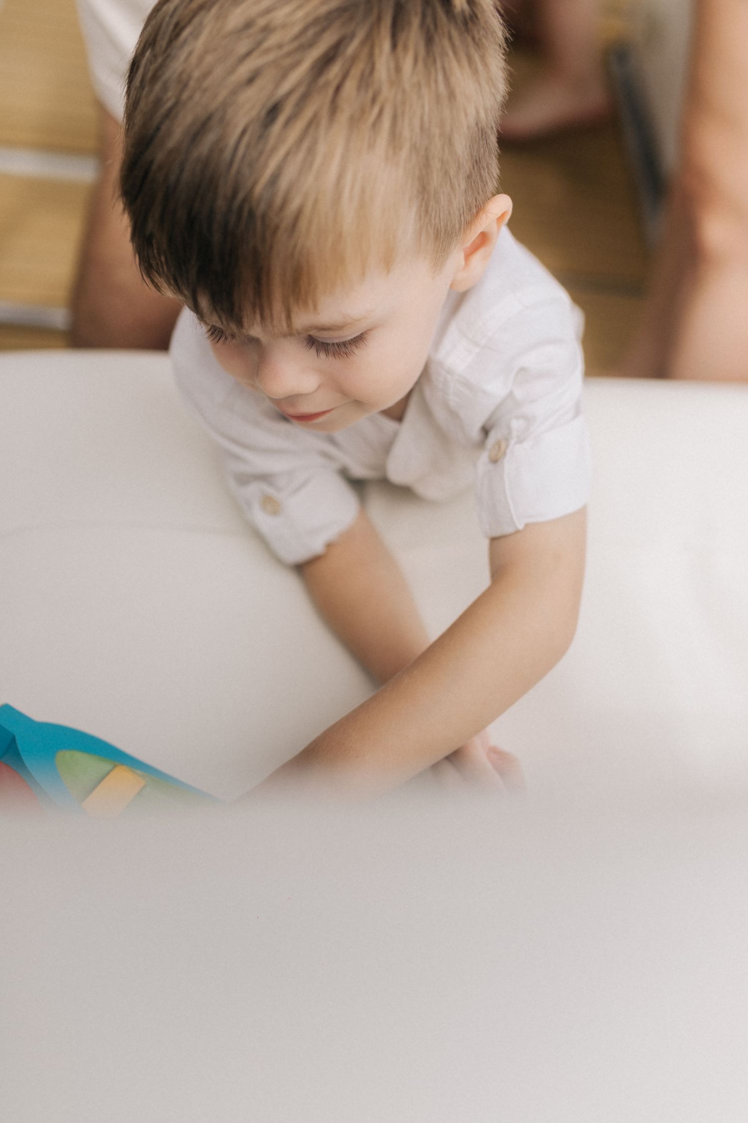 A child in white clothing leans down on a light colored surface.