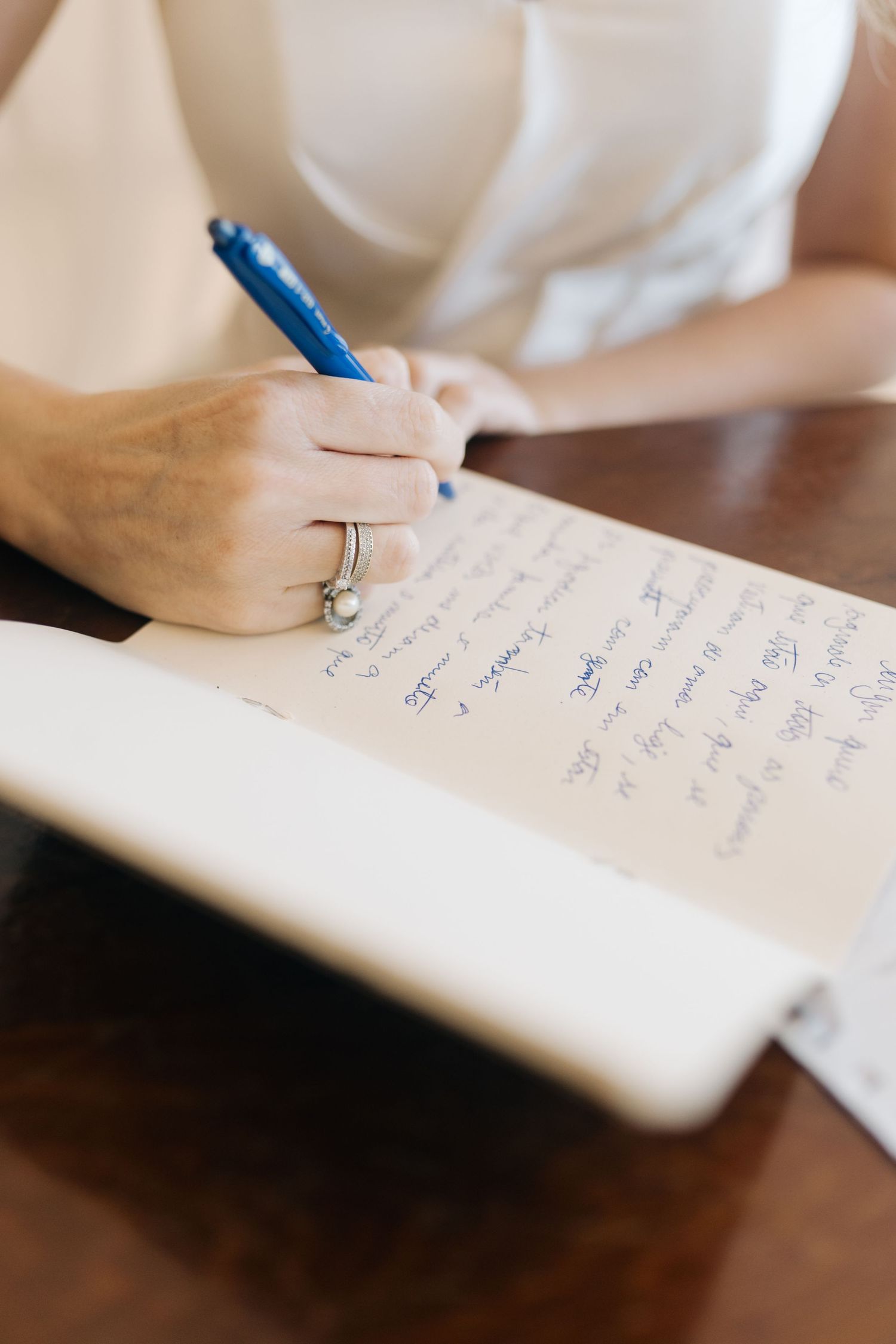 Close-up of hands writing in a notebook with blue pen while wearing a wedding ring.