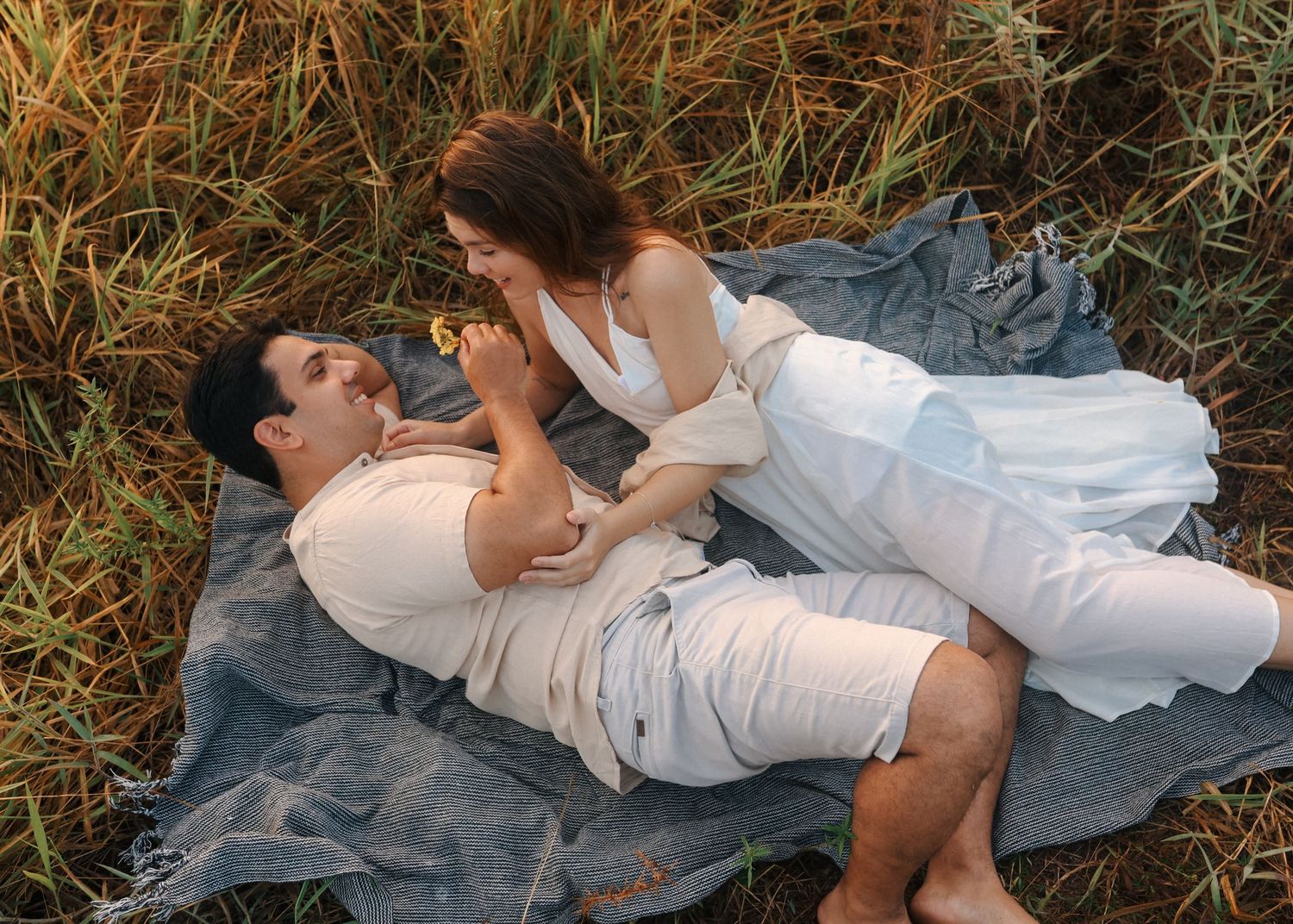 Loving couple embraces while lying on blanket in natural outdoor setting.
