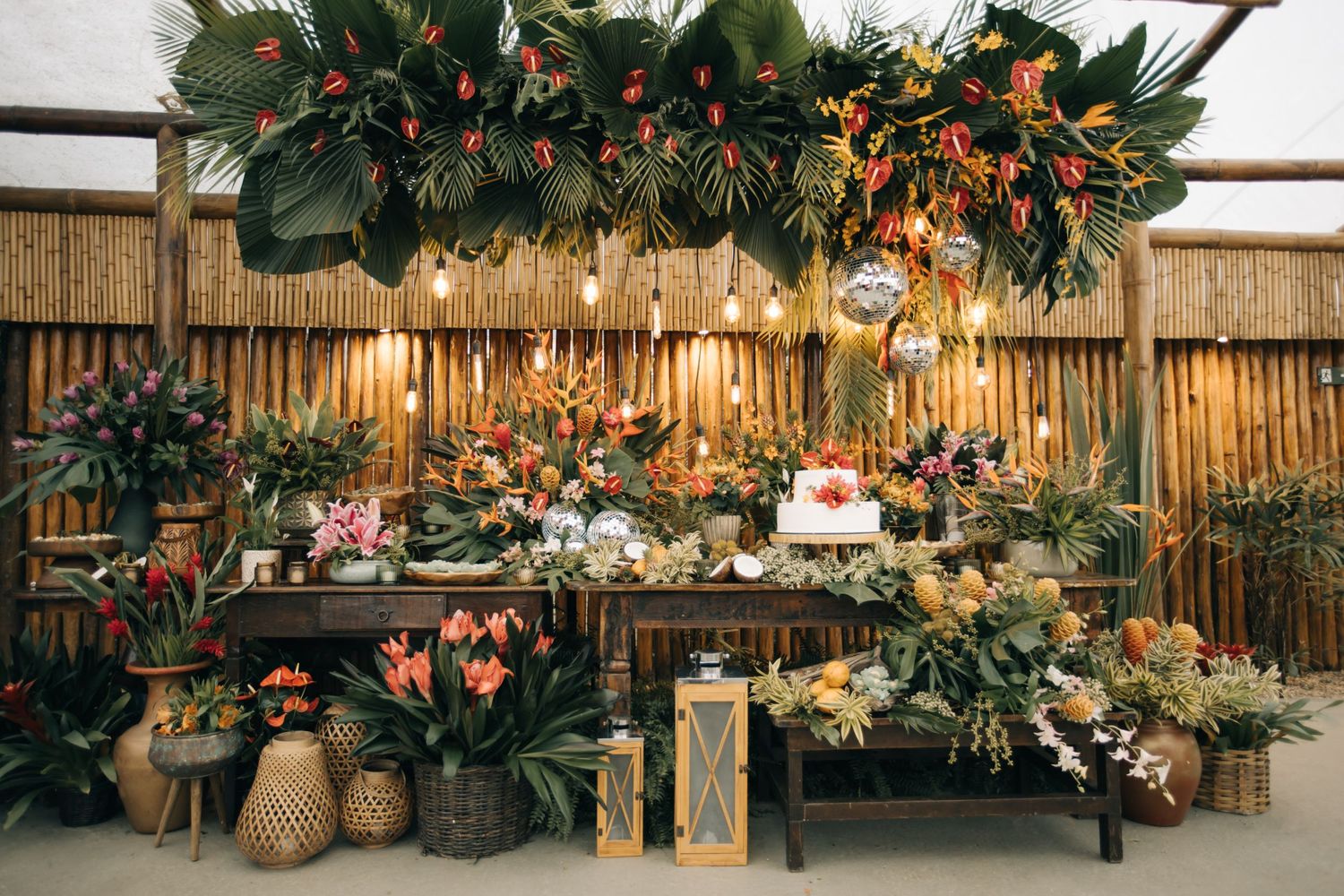 Rustic wedding reception table with bamboo backdrop and tropical floral arrangements.