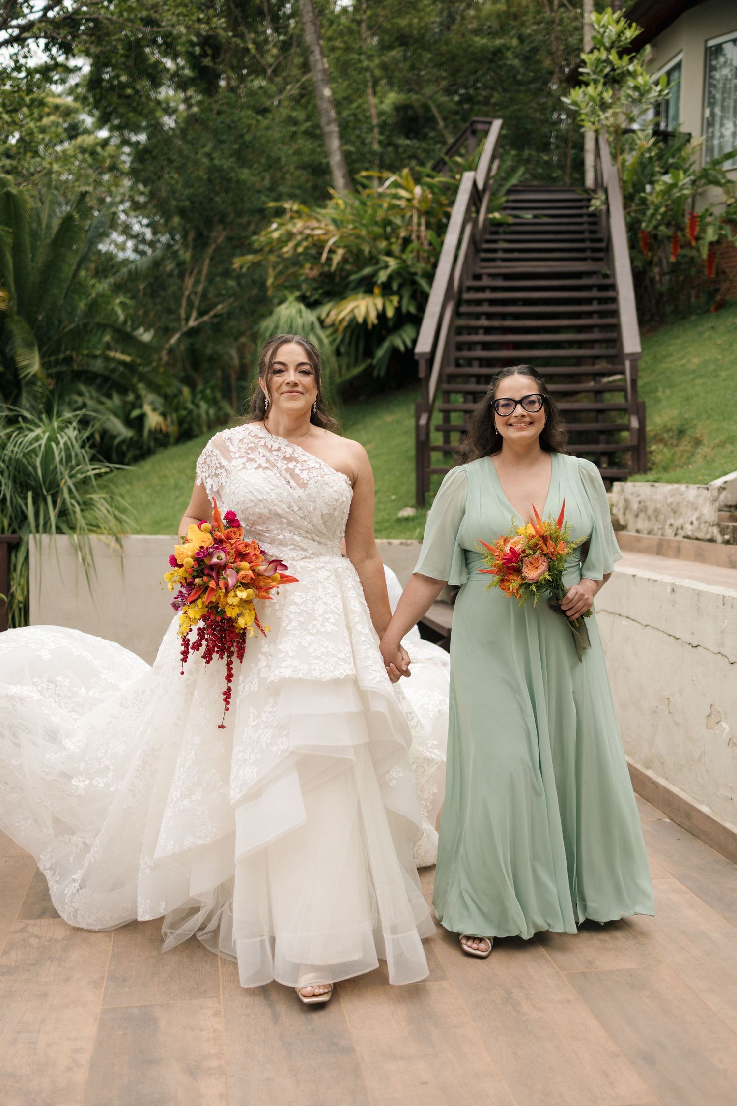 Bridesmaids in sage green dresses walking with bride in white gown holding autumn-colored bouquets.