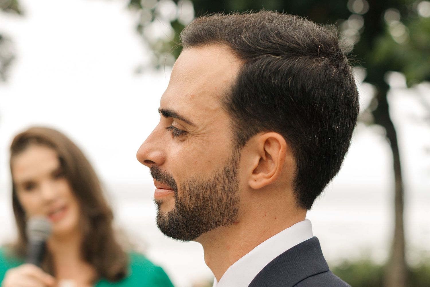 Side profile of groom in dark suit with green tie during outdoor ceremony.