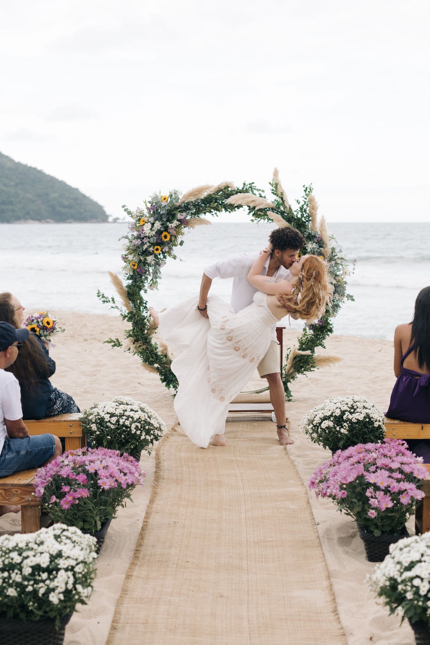 Couple sharing a romantic dip under a floral arch during their beach wedding ceremony.