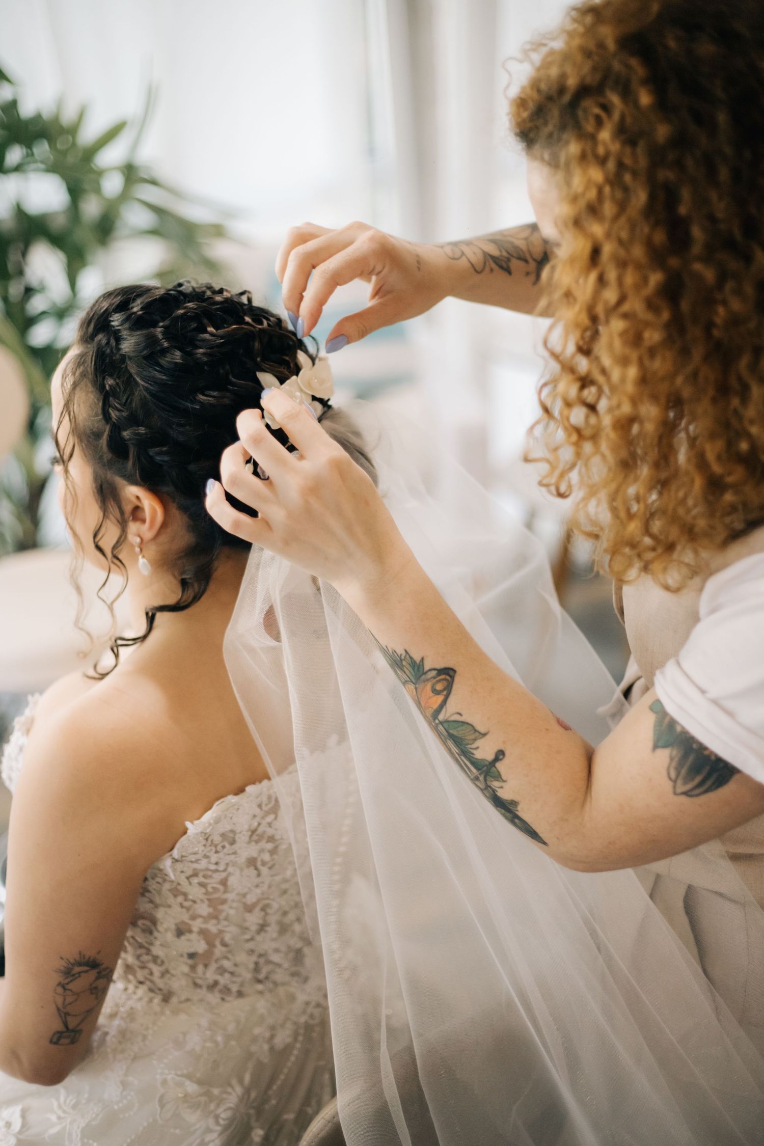 Close-up of stylist's tattooed hands arranging bride's hair and veil.
