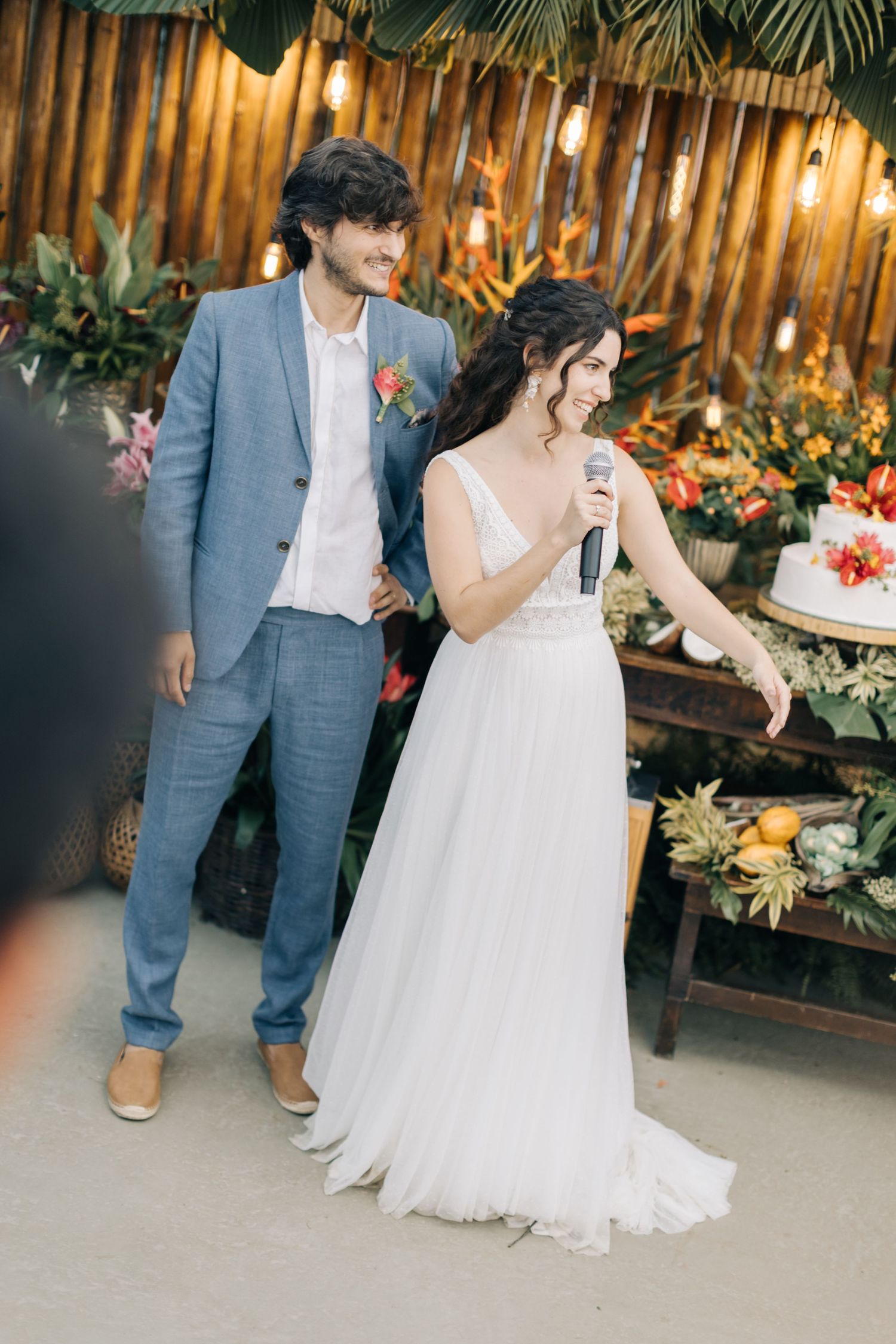 Wedding reception scene with bamboo backdrop and tropical floral arrangements.