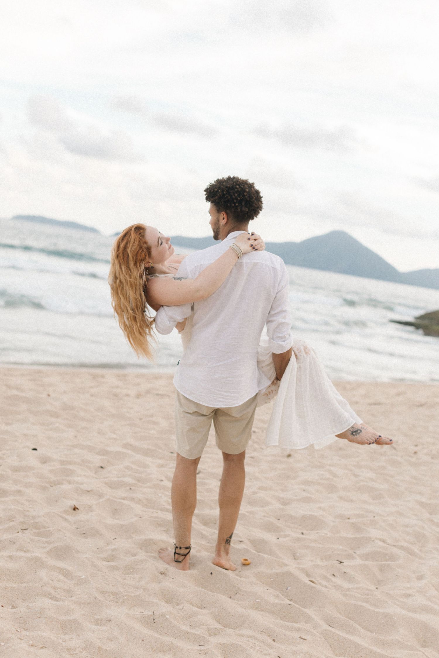 Couple dancing together on a sandy beach with mountains in the background.