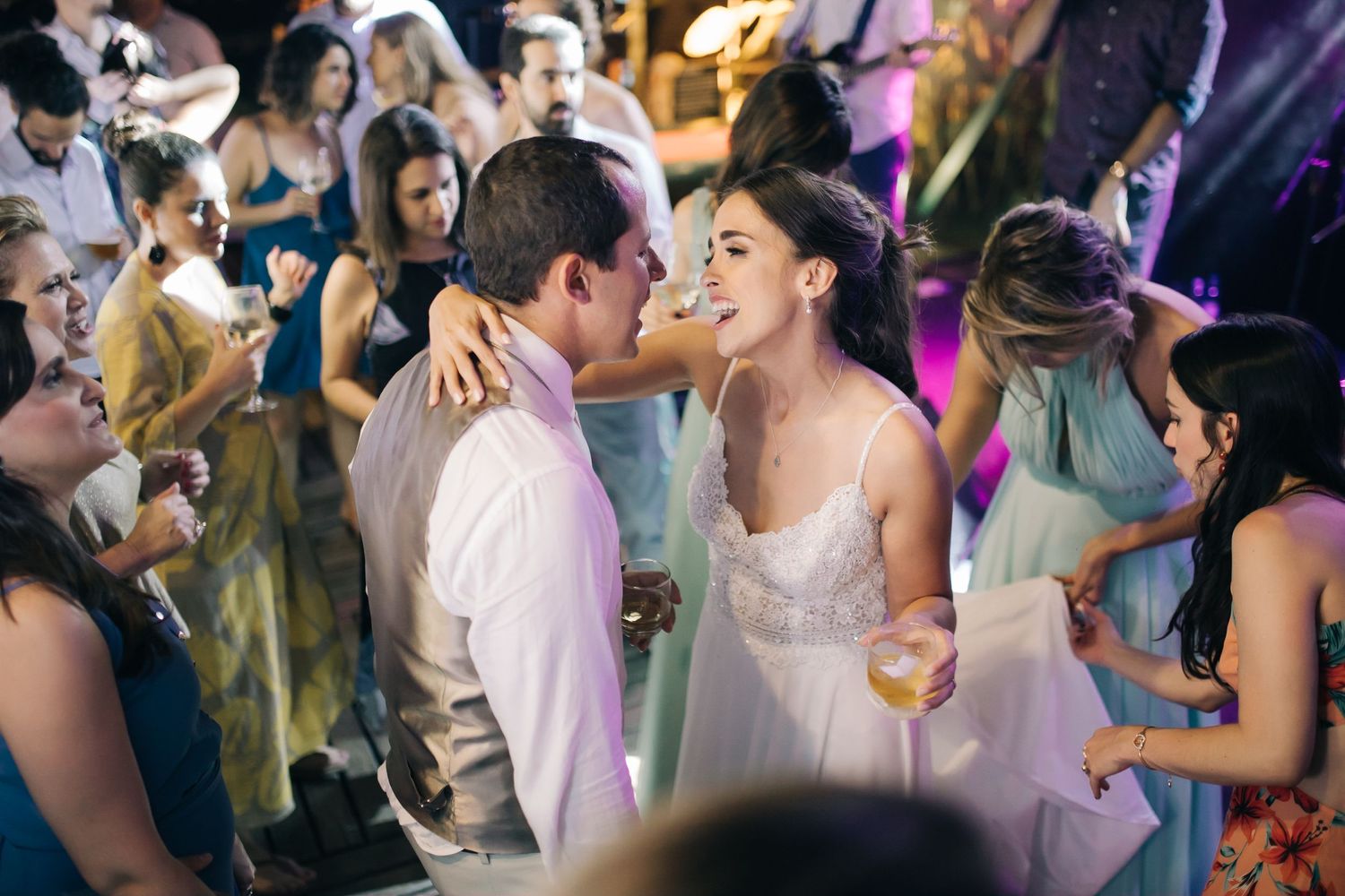 A couple shares a romantic moment on the dance floor surrounded by wedding guests at a reception.