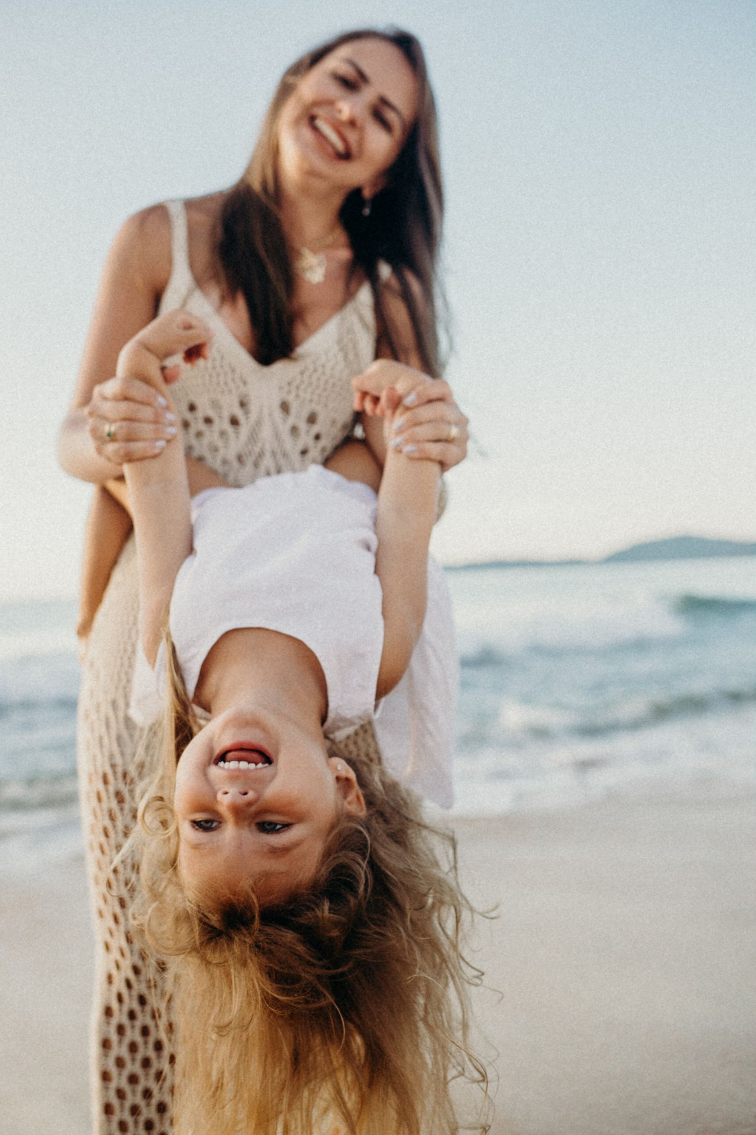 Candid beach portrait of playful moment with child suspended upside down by ocean.